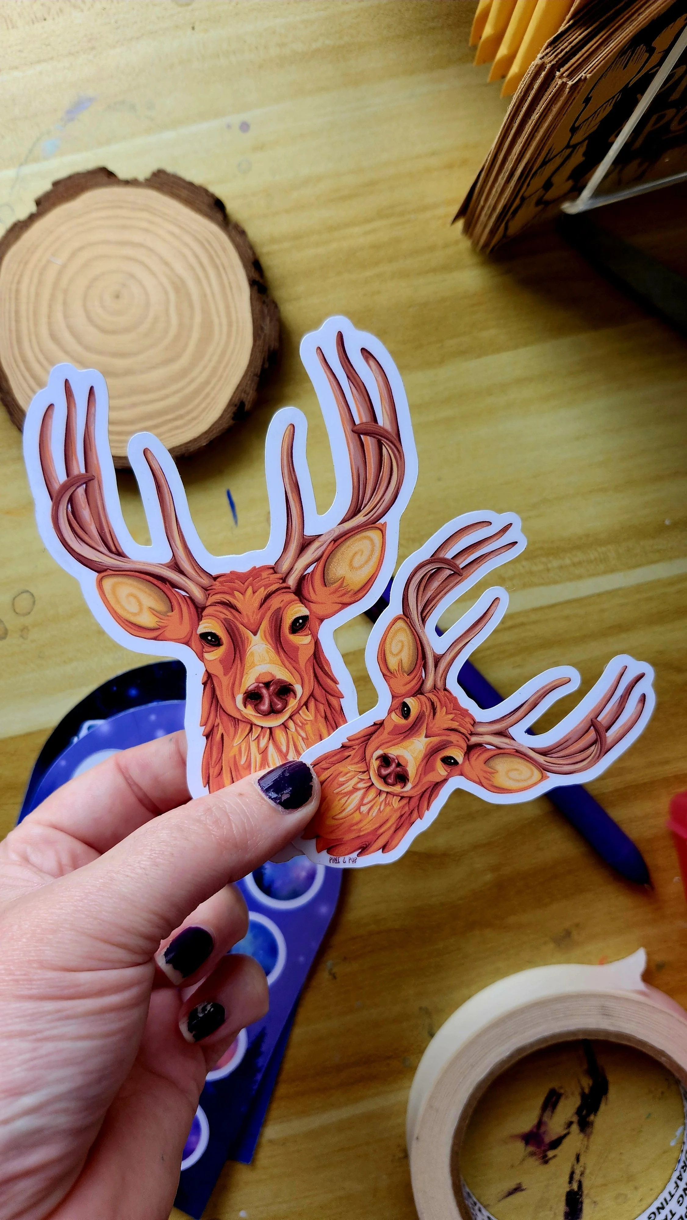 a hand holding the small size deer head sticker and the medium size sticker