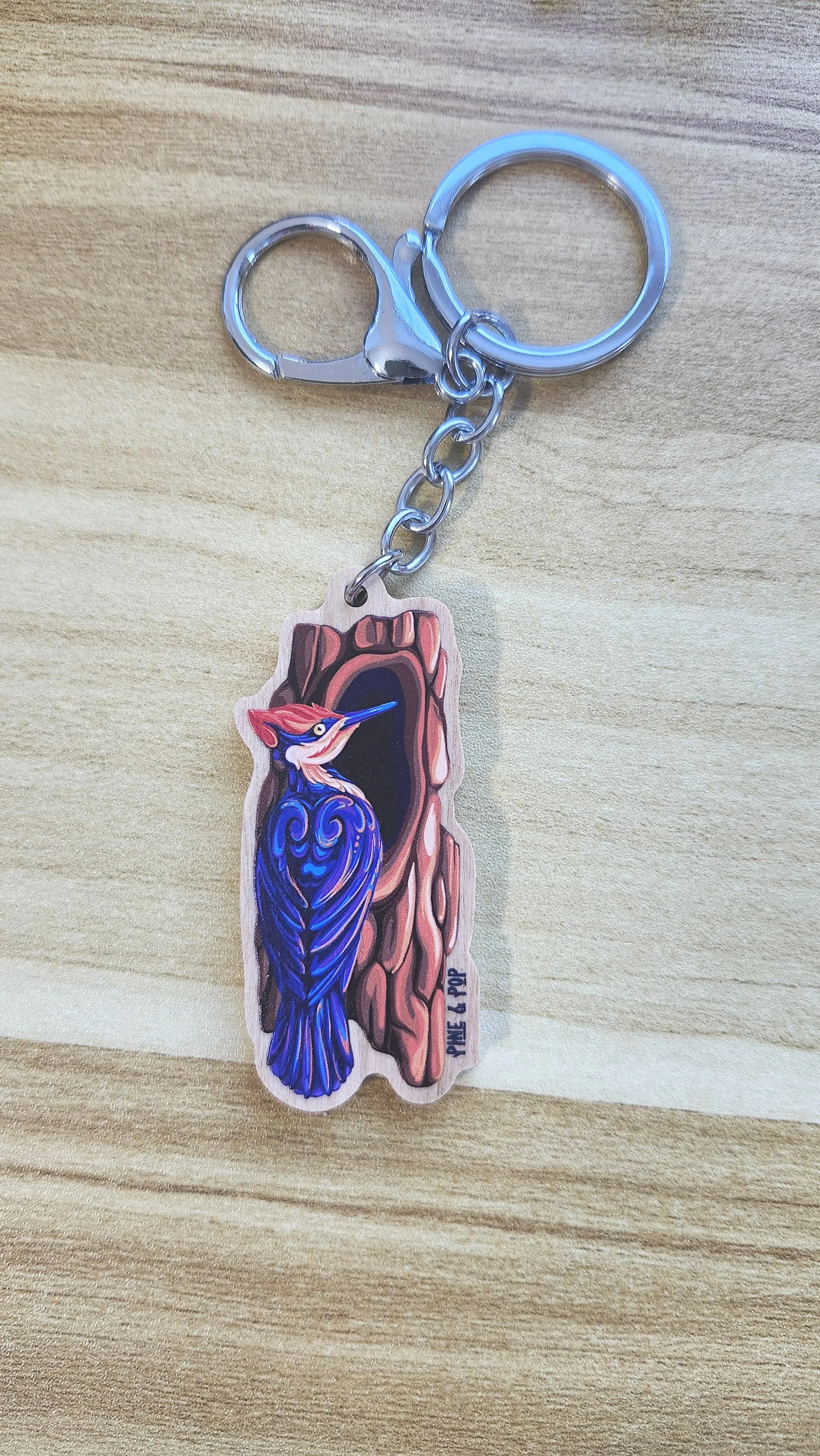 wooden keychain of pileated woodpecker next to tree hole made up of bold natural colors