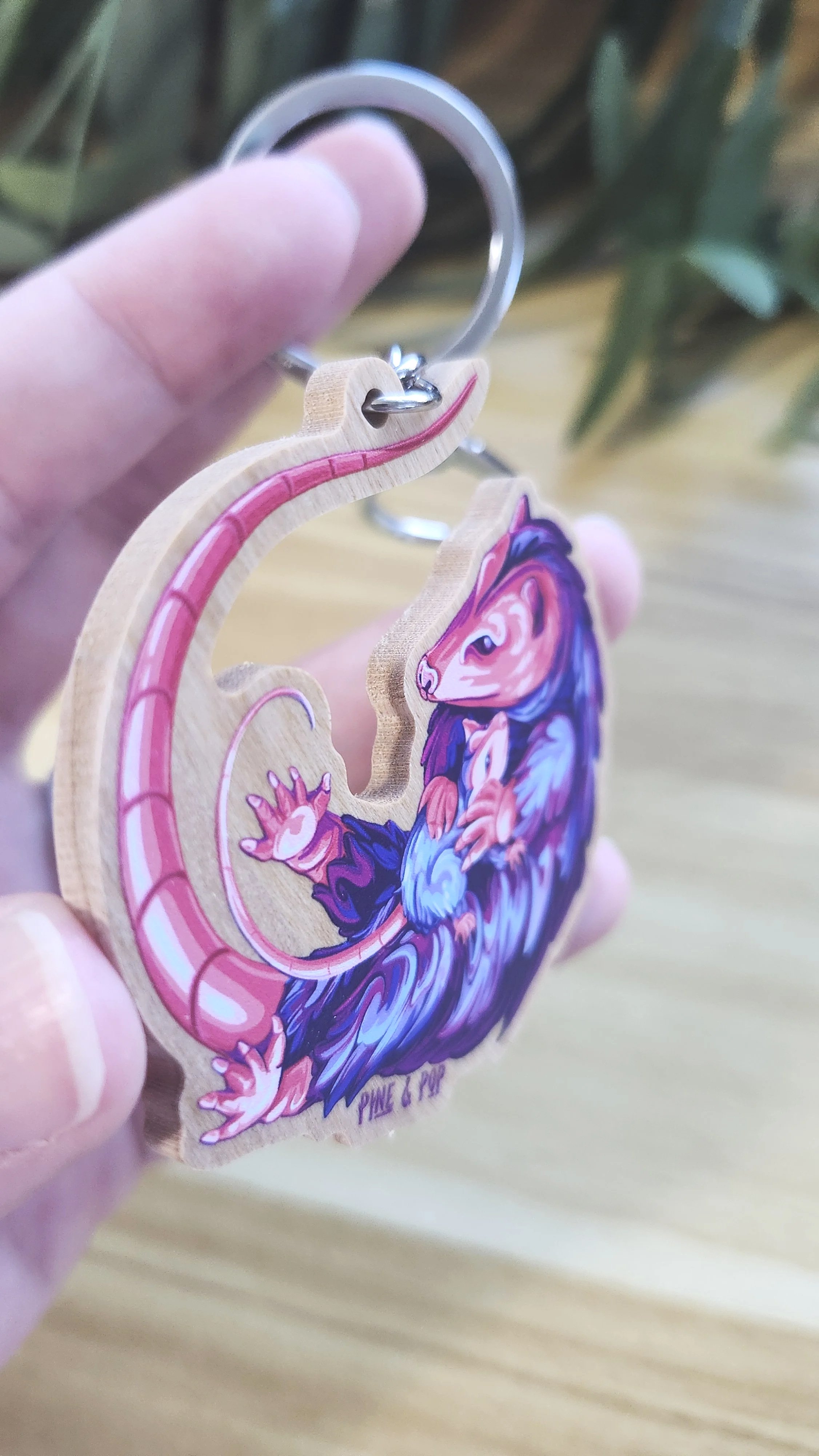 edge of wooden keychain of opossum holding baby opossum