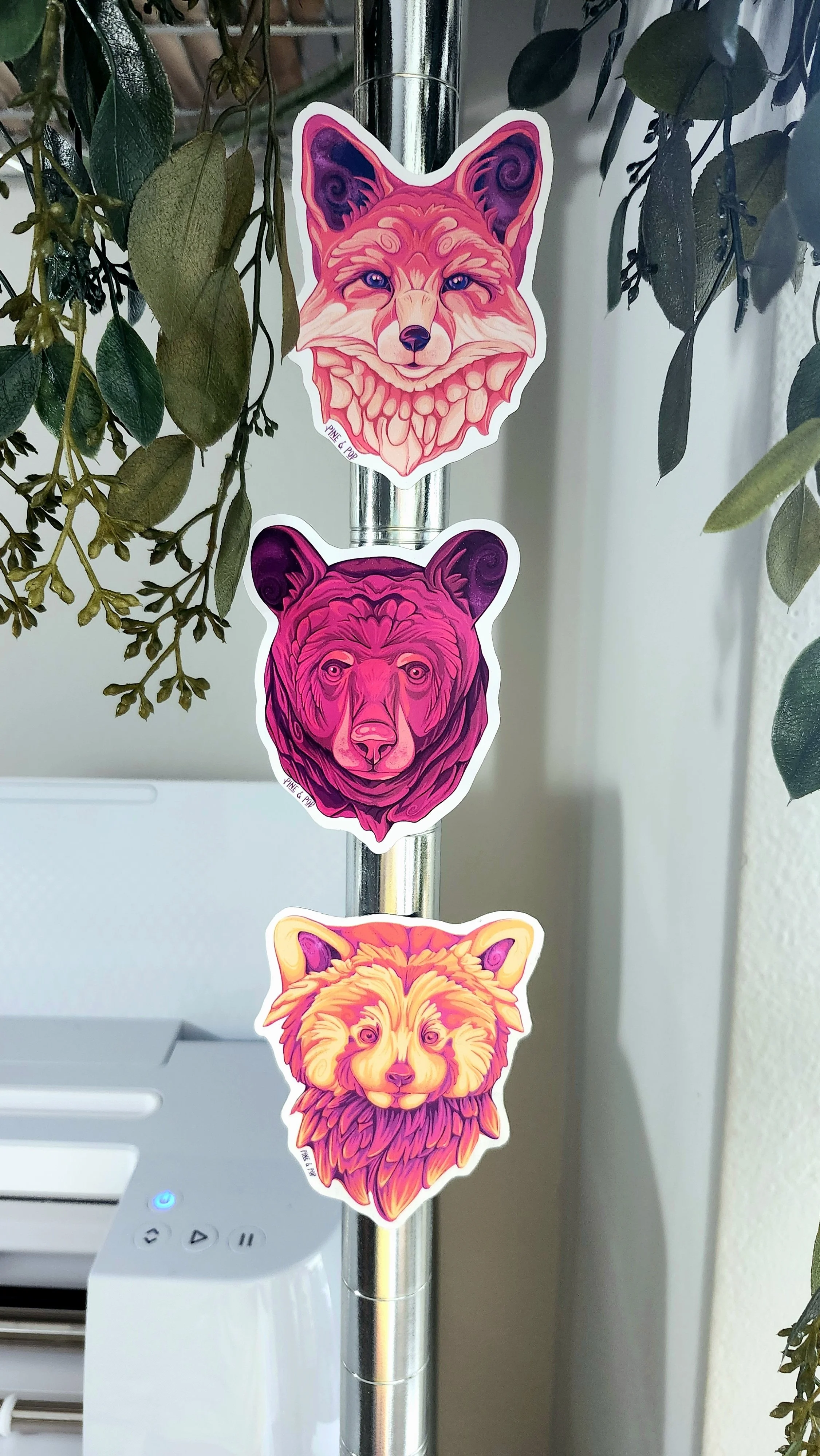 a red panda face magnet, a fox face magnet, and a bear face magnet stuck on a metal pole