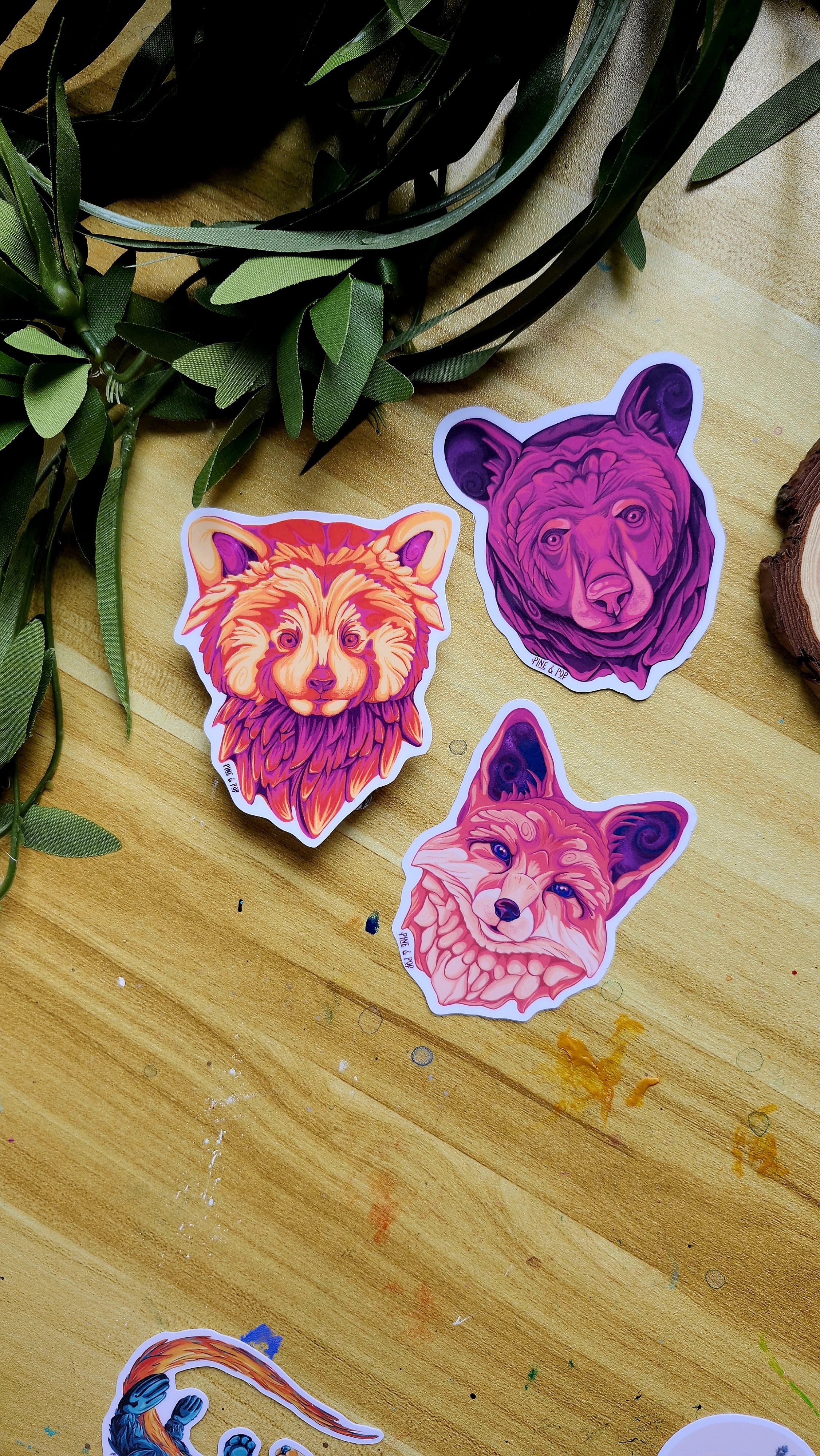 the red panda face sticker, the red fox face sticker, and the black bear face sticker laying on a wooden table