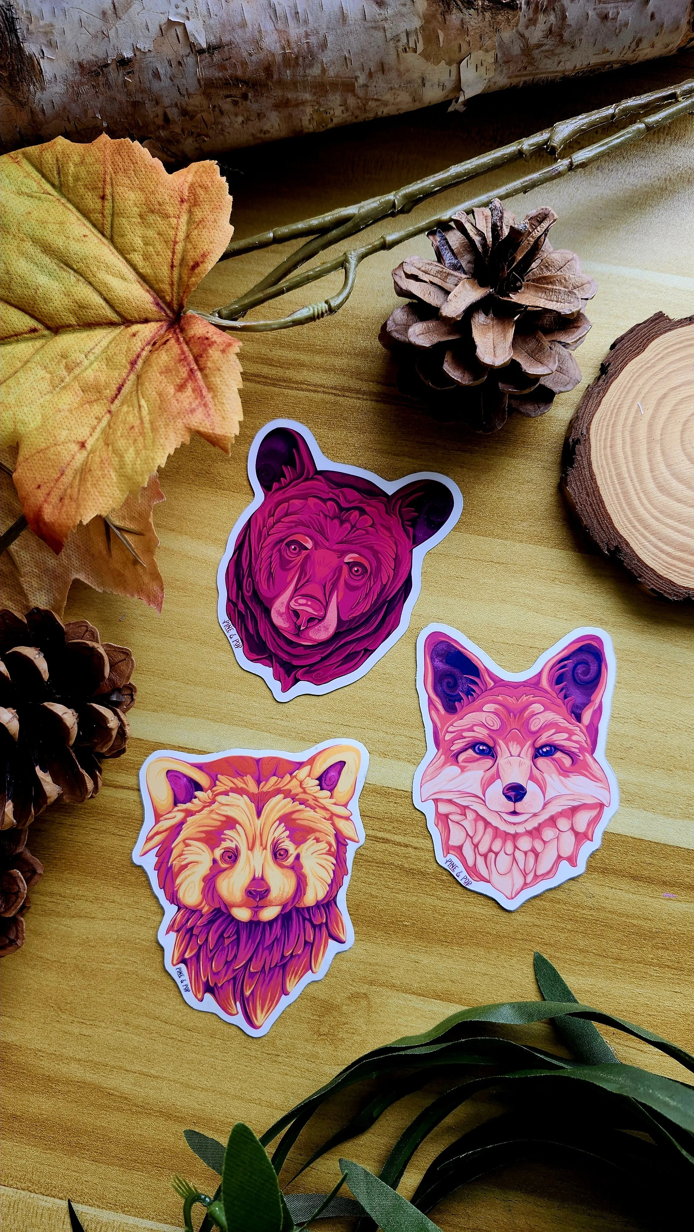 a red panda face magnet, fox face magnet, and bear face magnet laying together on a wooden table