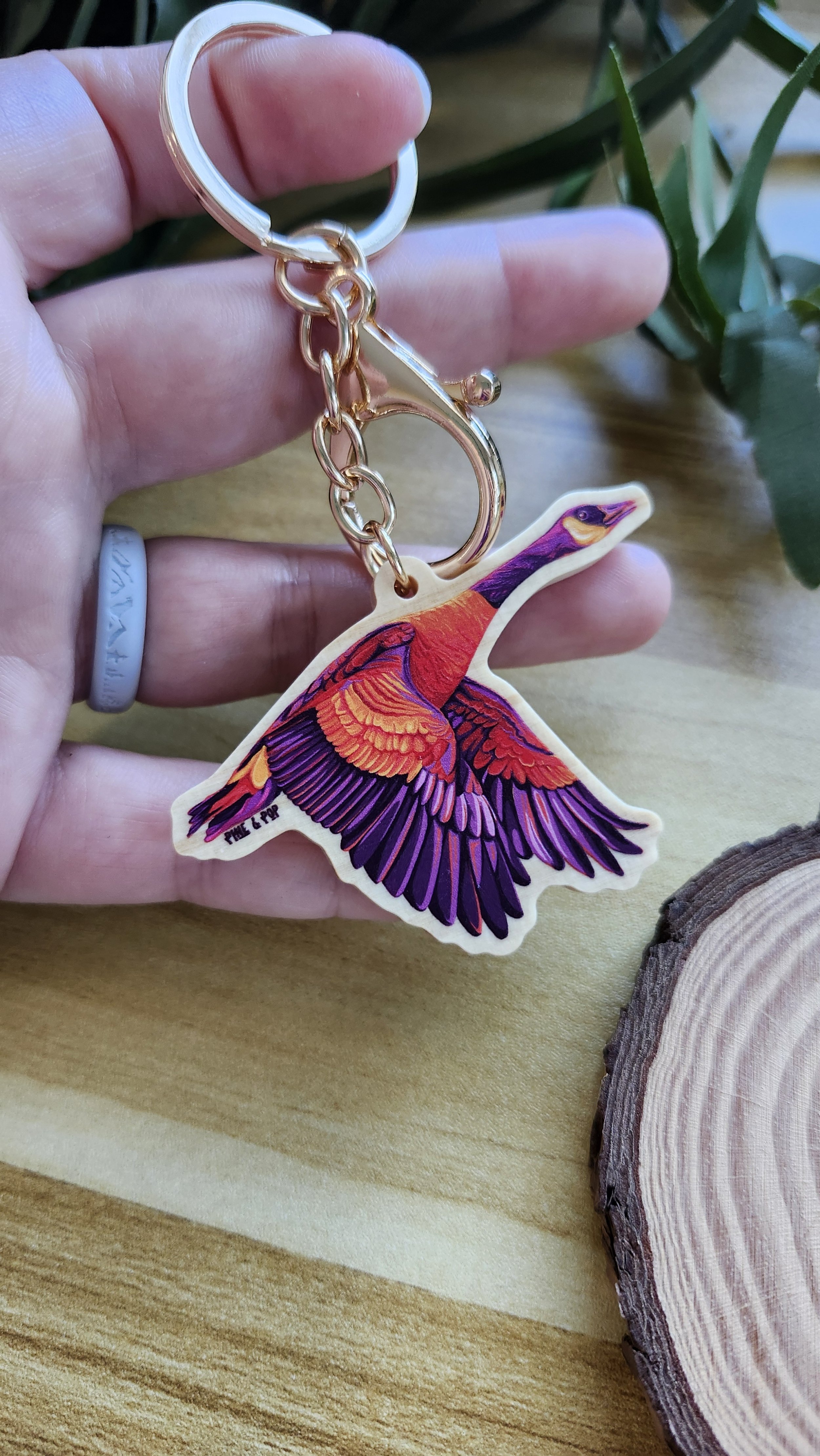 hand holding a wooden keychain of canada goose made up of yellow, orange, red, and purple colors