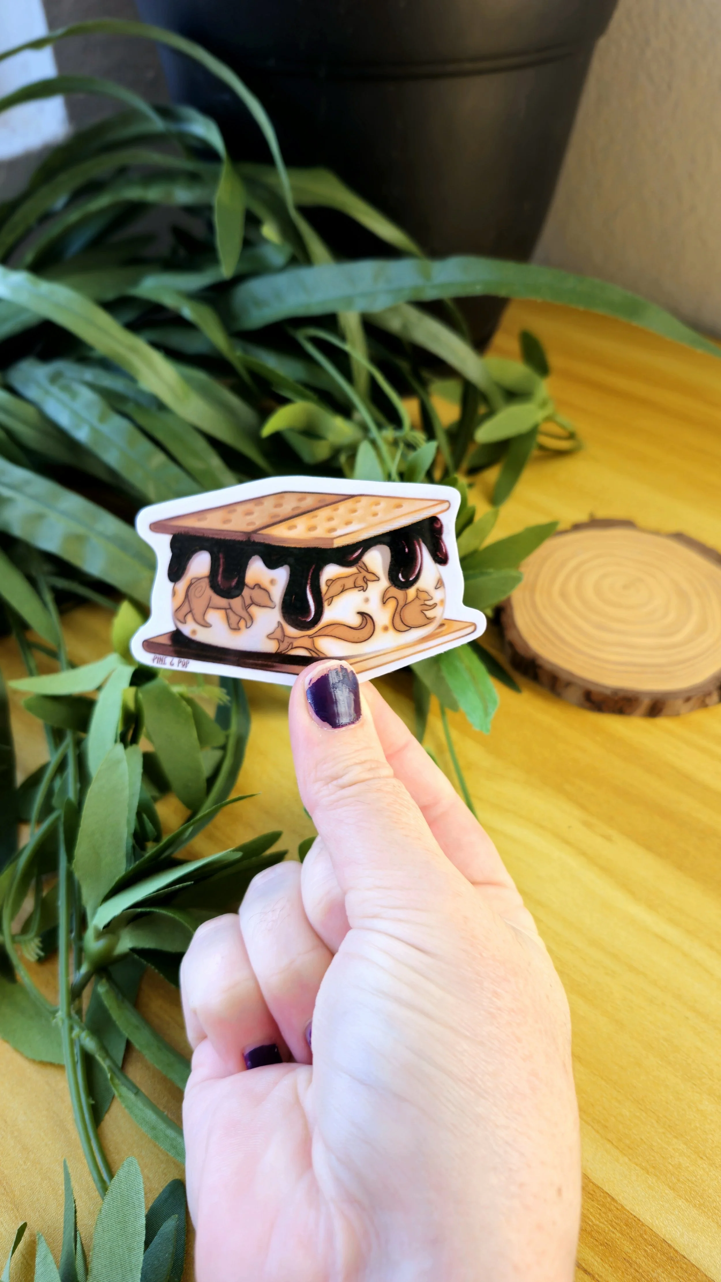 another view of a hand holding the s'more sticker with animal designs drawn on the middle marshmellow section