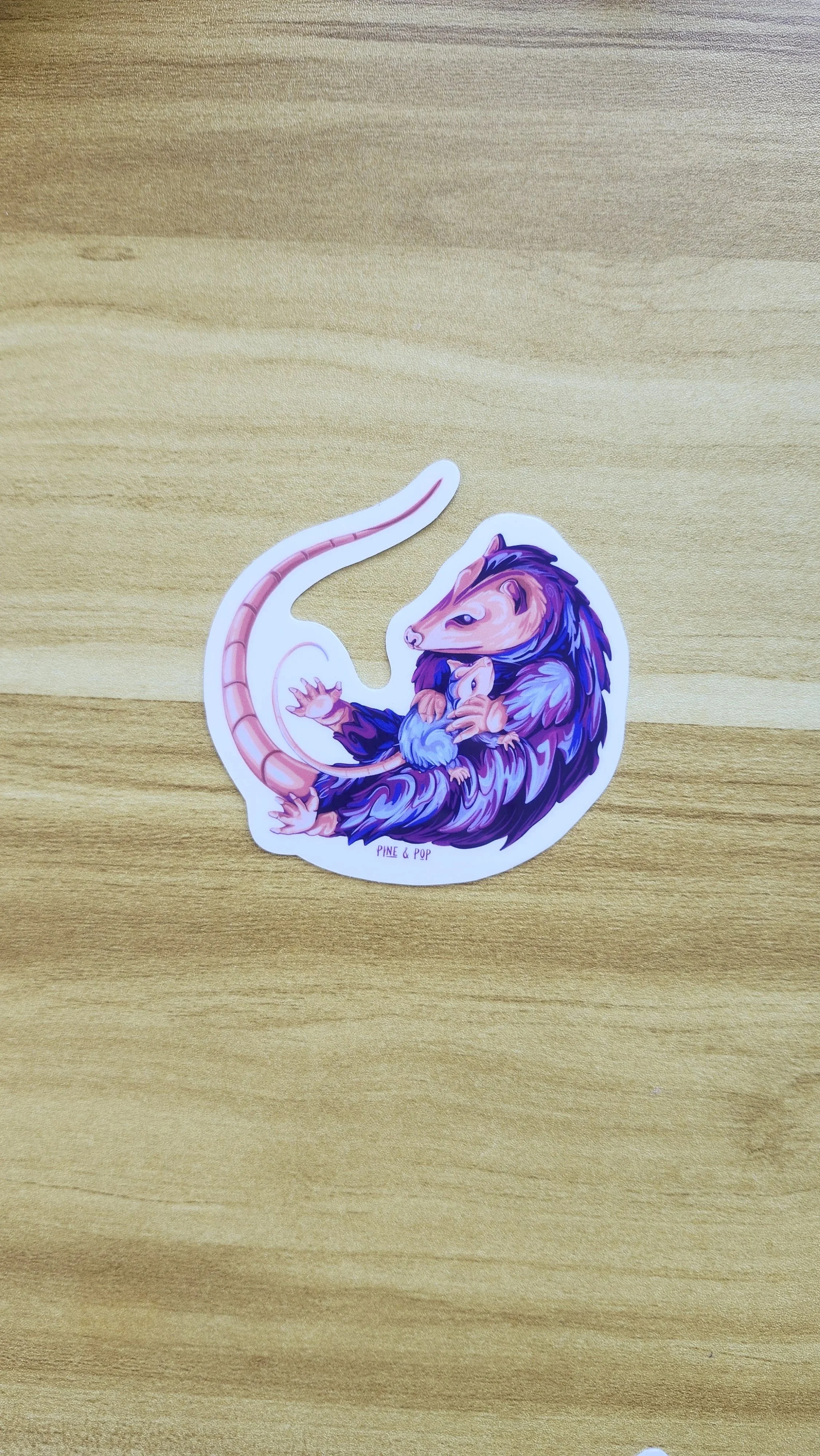 vinyl sticker of opossum that is holding a baby opossum made with bright blue, purple, pink, and coral colors