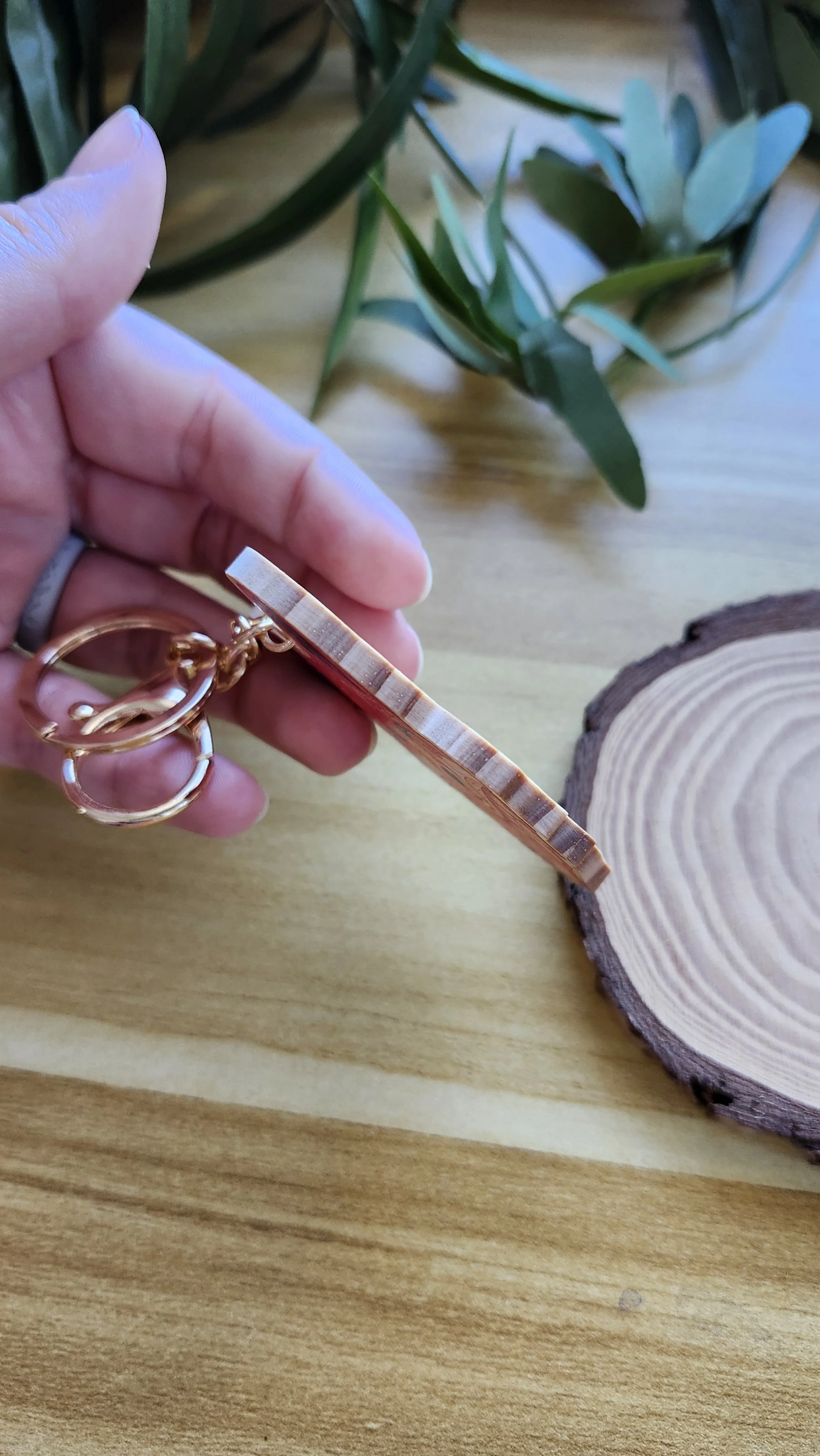 a hand holding the keychain to the side to show the wooden edge and the thickness