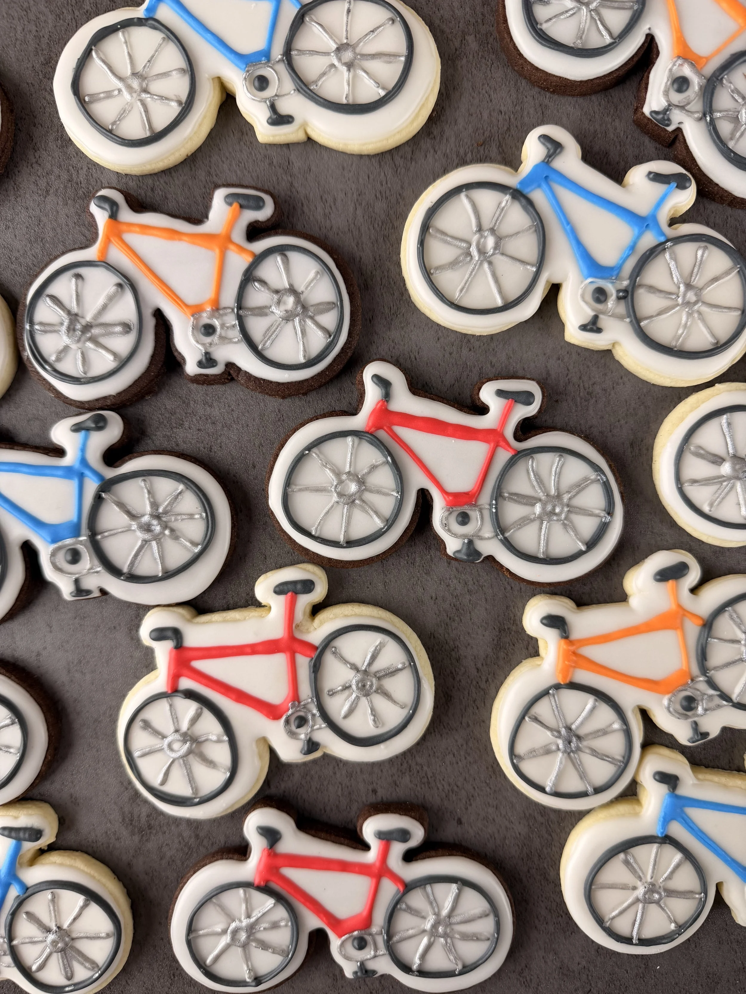 Decorative cookies shaped like bicycles, decorated with icing in colors including blue, red, orange, and black.