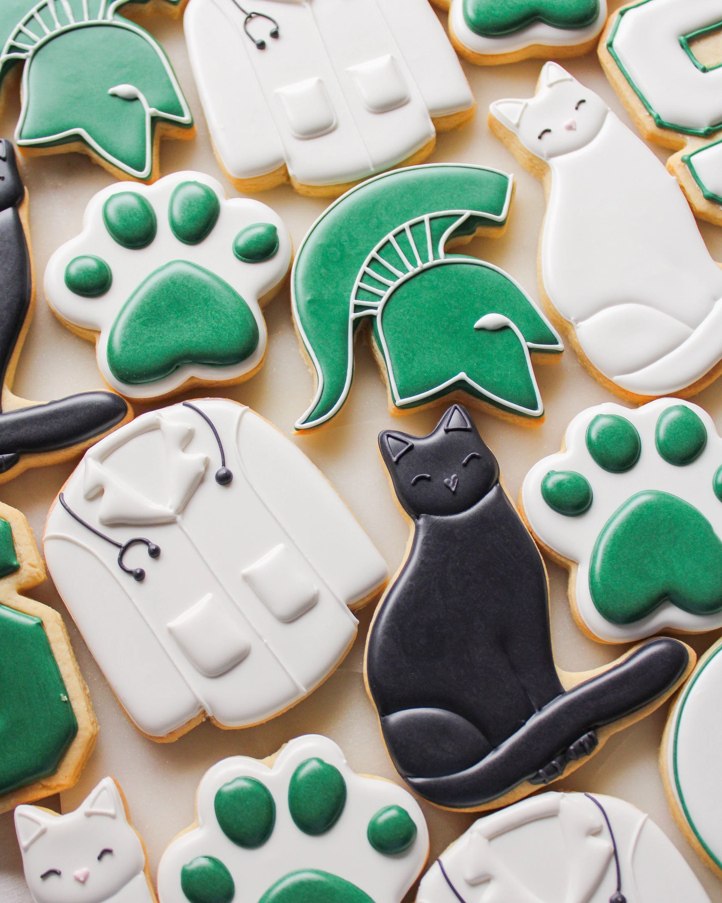 Decorated cookies for MSU vet white coat, featuring cats, spartan, white coat,  paw prints designs in green and white