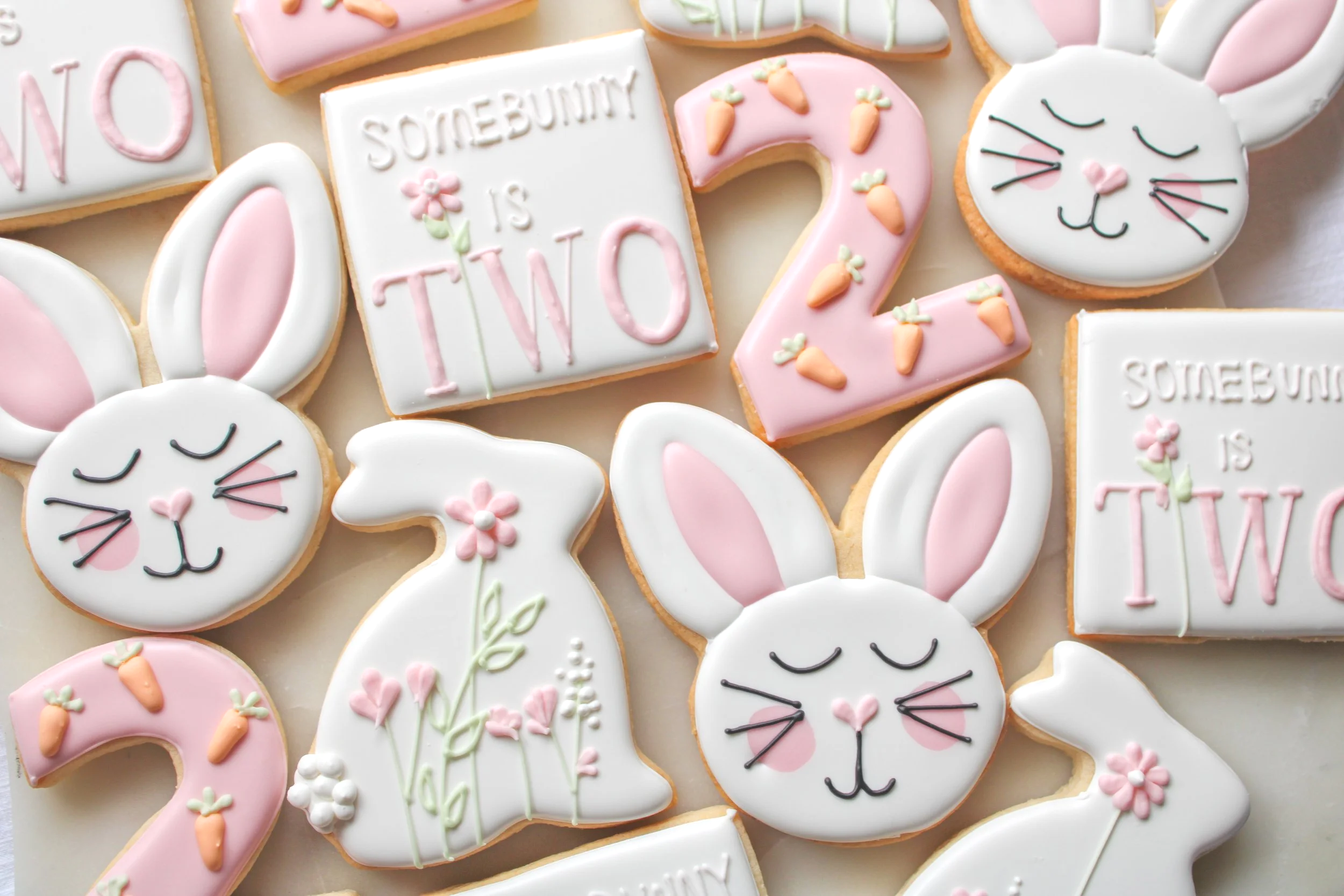 Birthday decorated cookies featuring bunny faces, rabbits, numbers two, carrots, and phrase 'SomeBunny is Two' with pink, white, and pastel-colored icing.