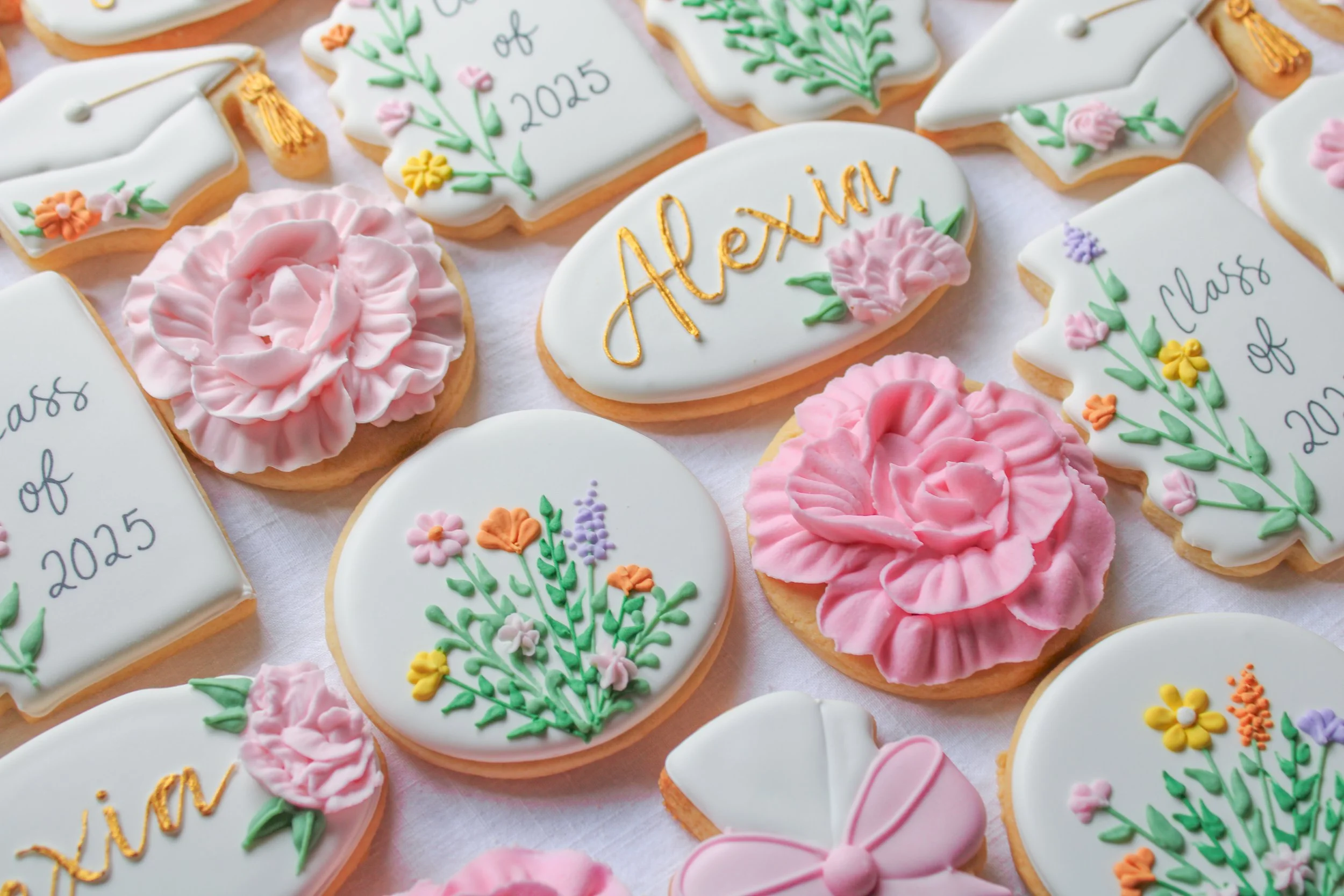 Decorated cookies with floral designs, pink rosettes, and text for a graduating class of 2025, featuring the name Alexia.