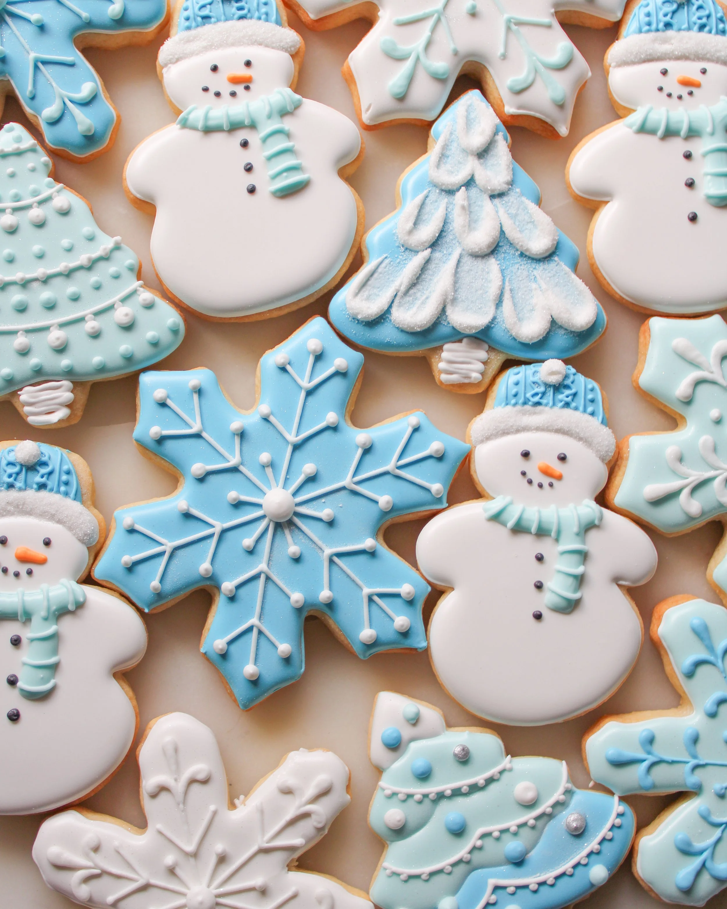 Assorted Christmas sugar cookies decorated with winter themes: snowmen with scarves and hats, snowflakes, and Christmas trees, in white, blue, and pastel colors.