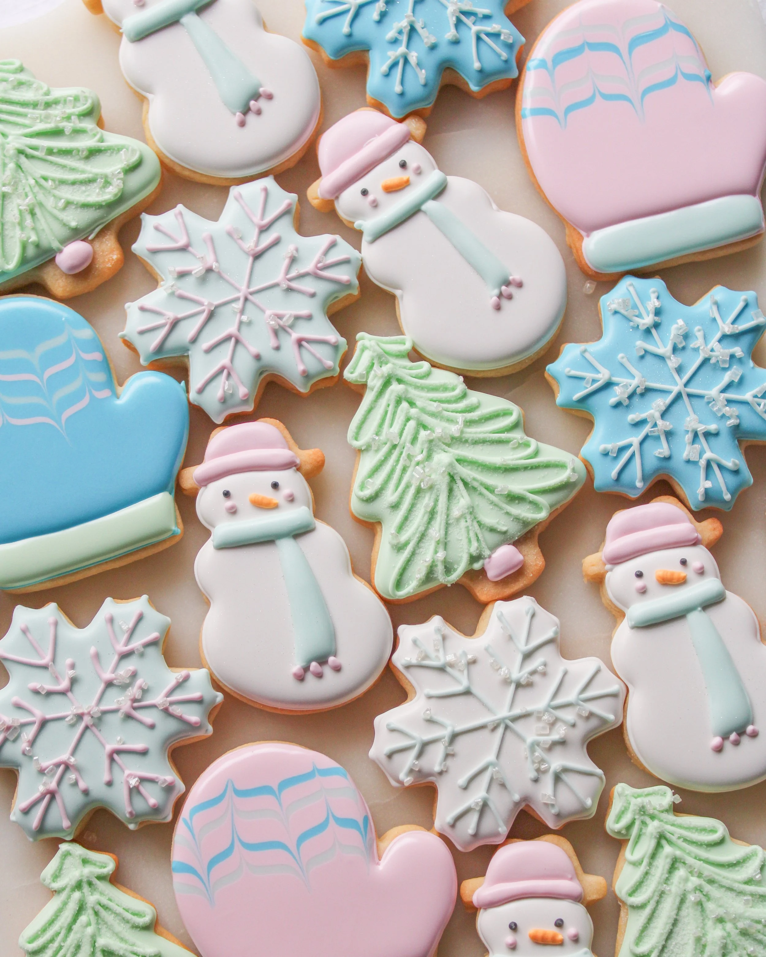 Assorted decorated Christmas cookies, including snowmen, snowflakes, Christmas trees, and hearts with pastel colored icing.