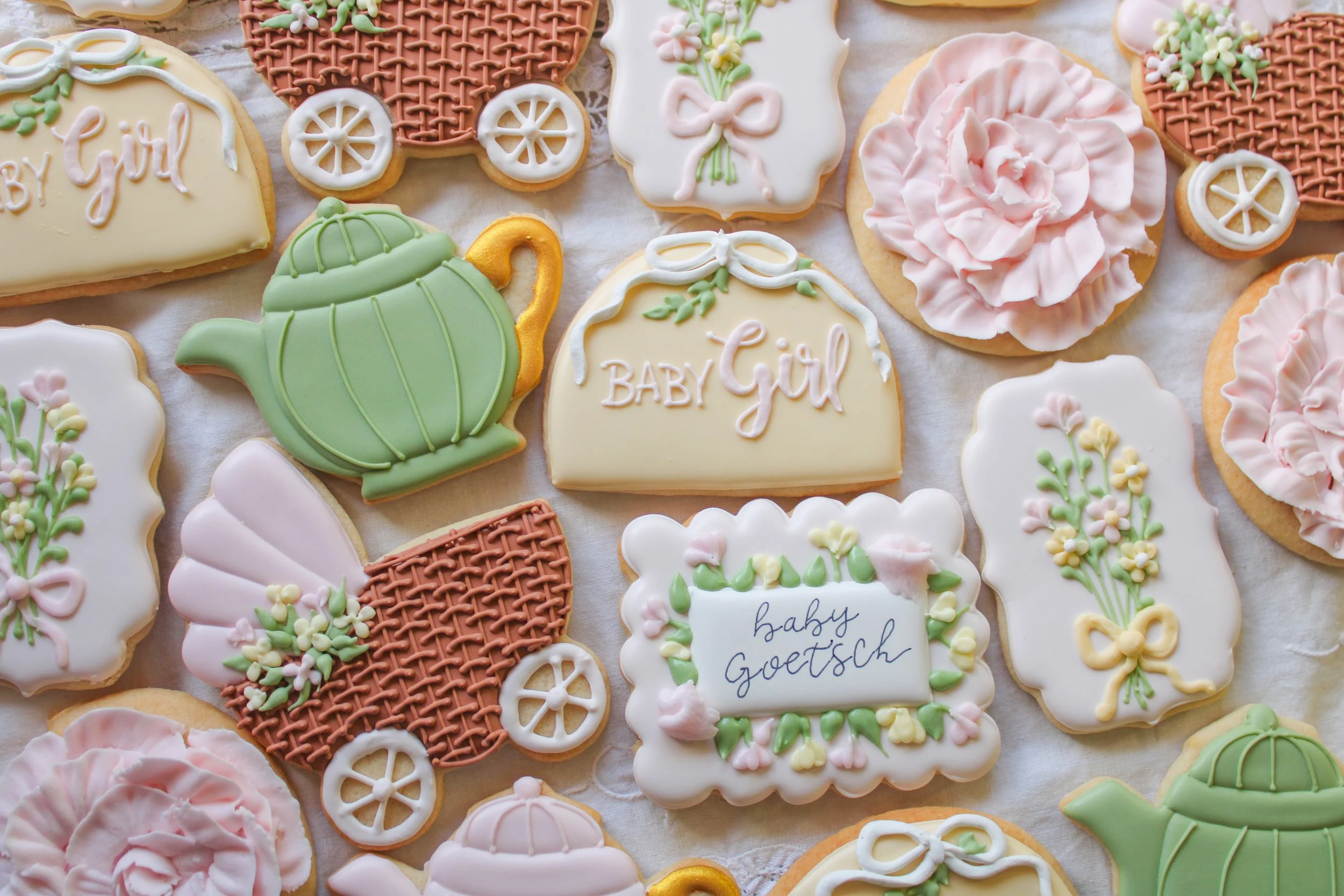 Decorative cookies with baby shower themes, including teapots, baby carriages, flowers, and the words 'Baby Girl' and 'baby Goethe' in pastel colors.