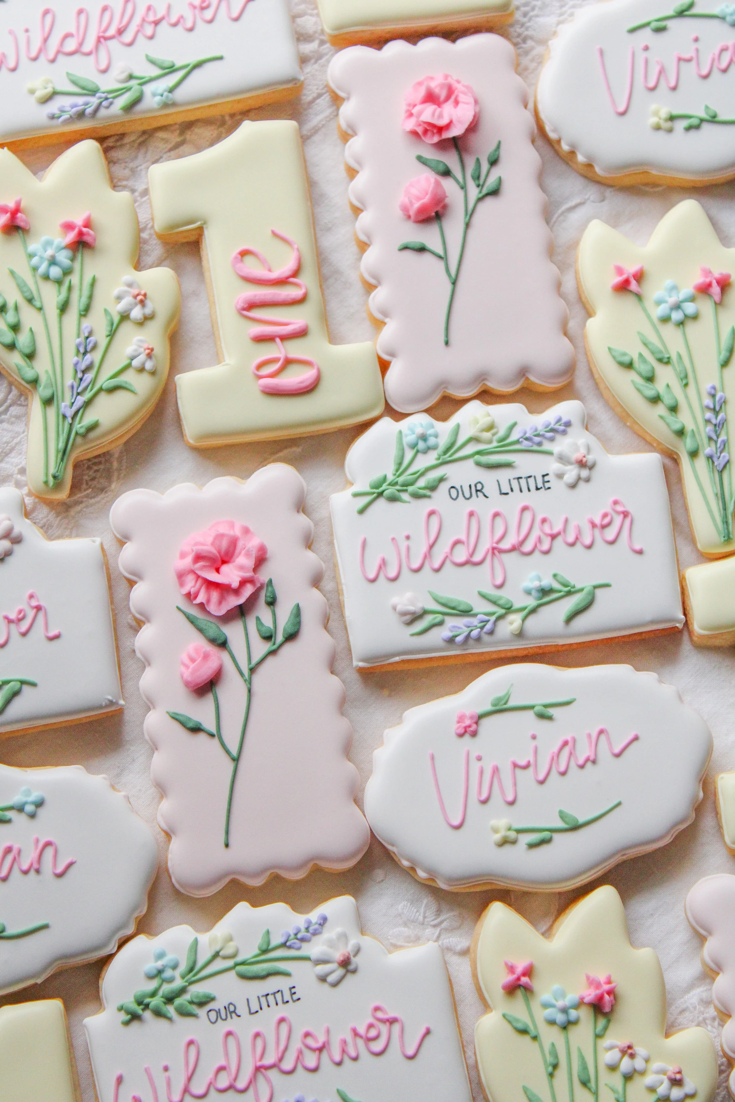 Decorated sugar cookies with floral designs and the words "Our Little Wildflower" and the name "Vivian" written on them.