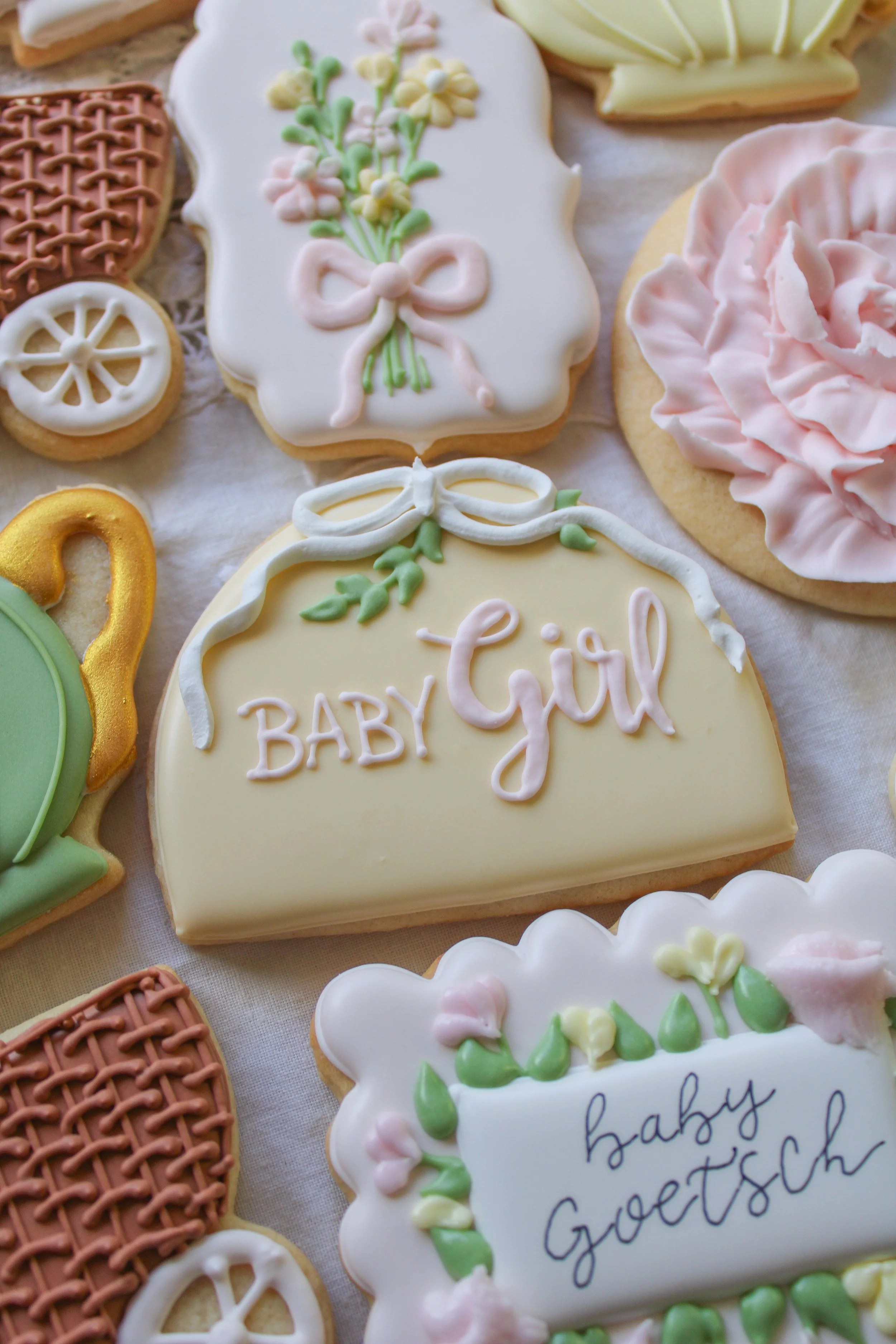 Decorated cookies for a baby girl, with pastel colors and phrases like 'Baby Girl' and 'Baby Goots,' featuring flowers, bows, and baby-themed designs.