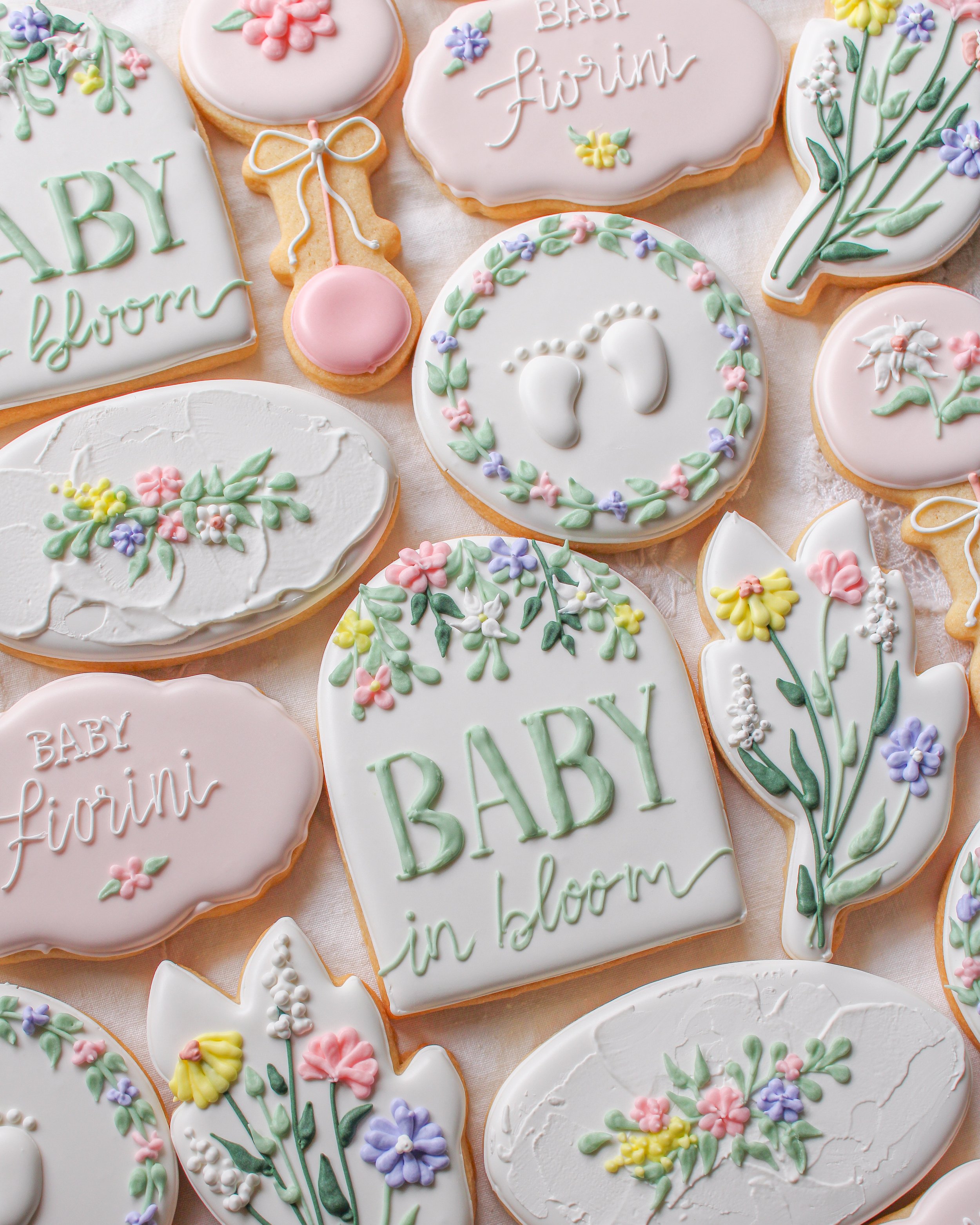 Assorted baby shower cookies decorated with pastel-colored icing, floral patterns, and messages like "Baby in bloom" 