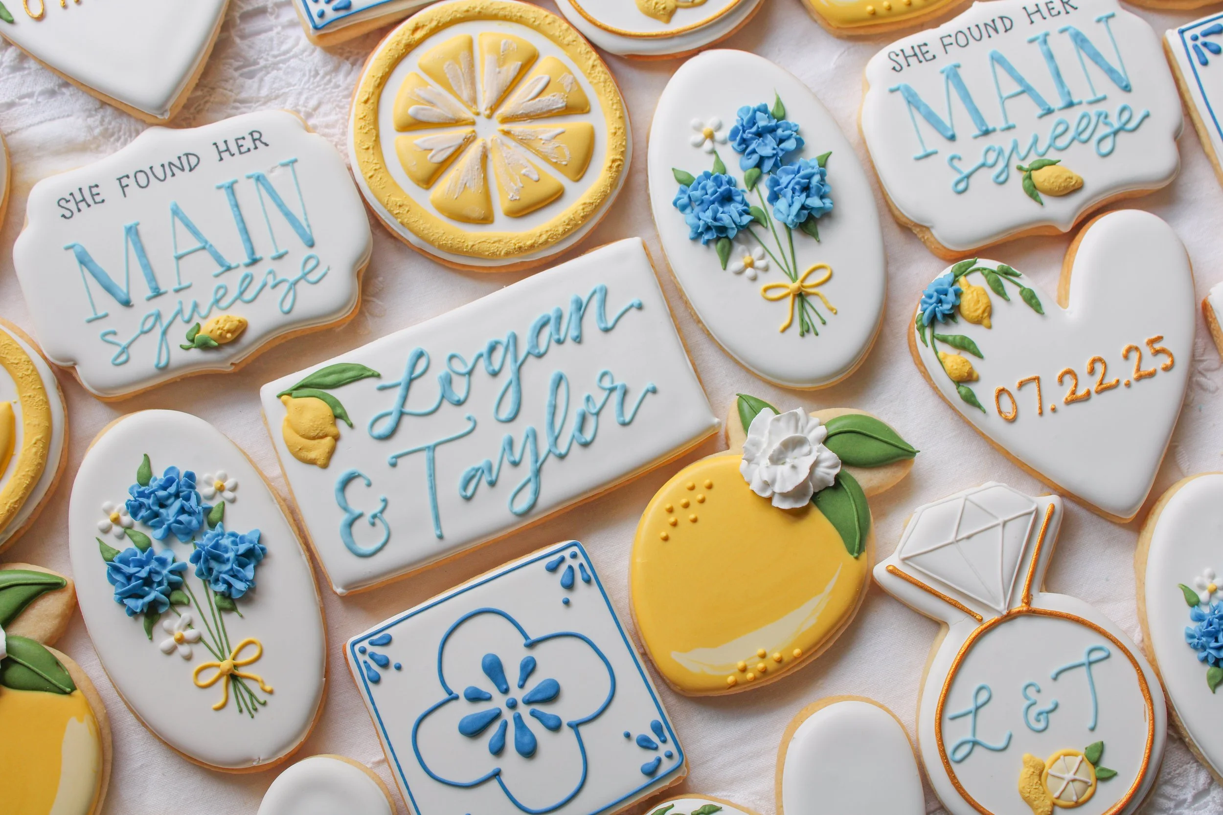 Collection of decorated cookies with lemon slices, flowers, and personalized messages, featuring blue, yellow, and white icing details for a celebration.