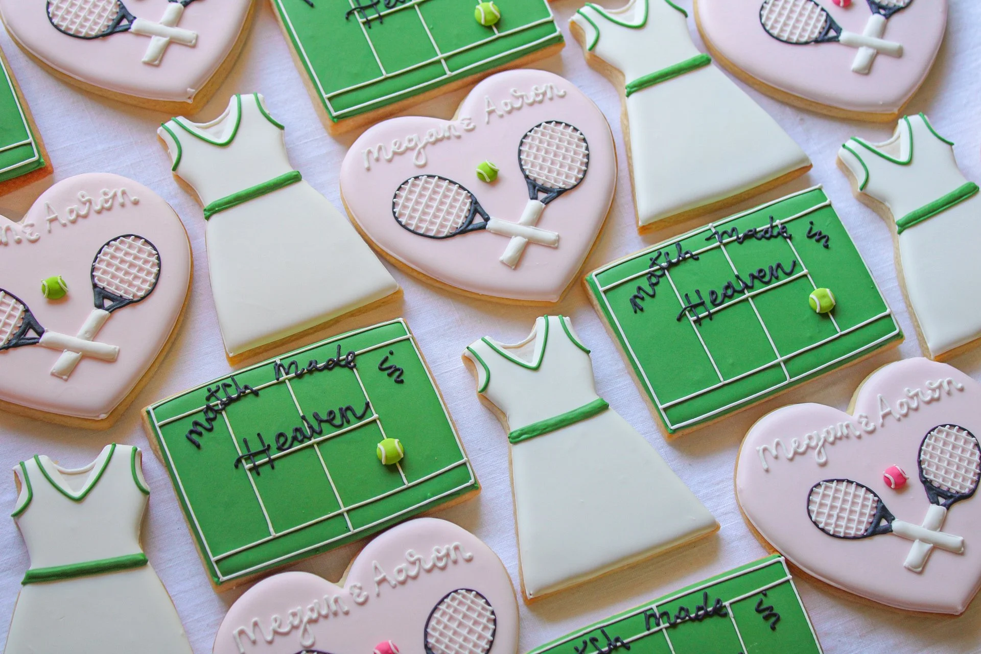 Decorative cookies shaped like tennis hearts, tennis dresses, and tennis courts with writing and tennis ball decorations for a wedding or celebration.