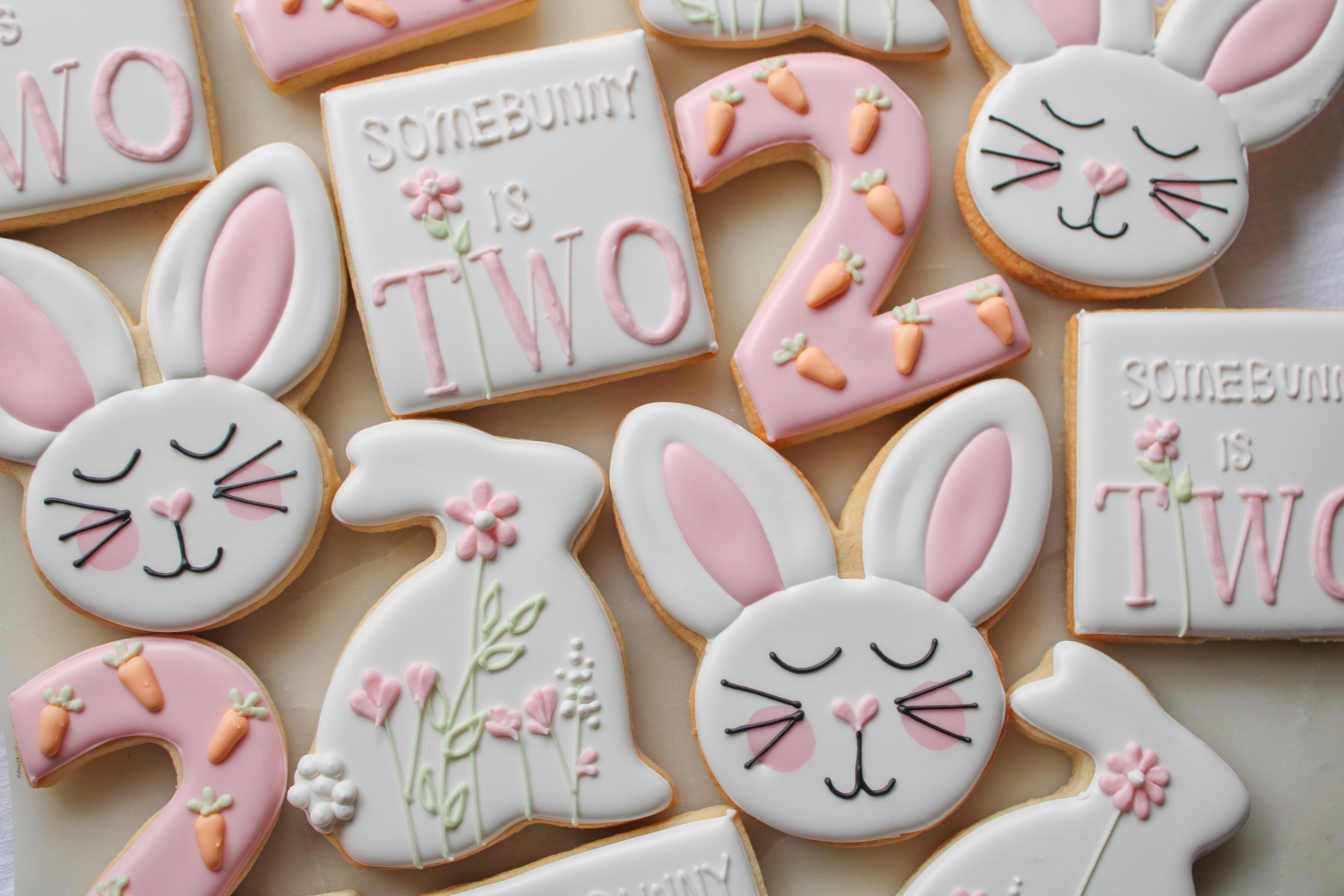 Birthday decorated cookies featuring bunny faces, rabbits, numbers two, carrots, and phrase 'SomeBunny is Two' with pink, white, and pastel-colored icing.