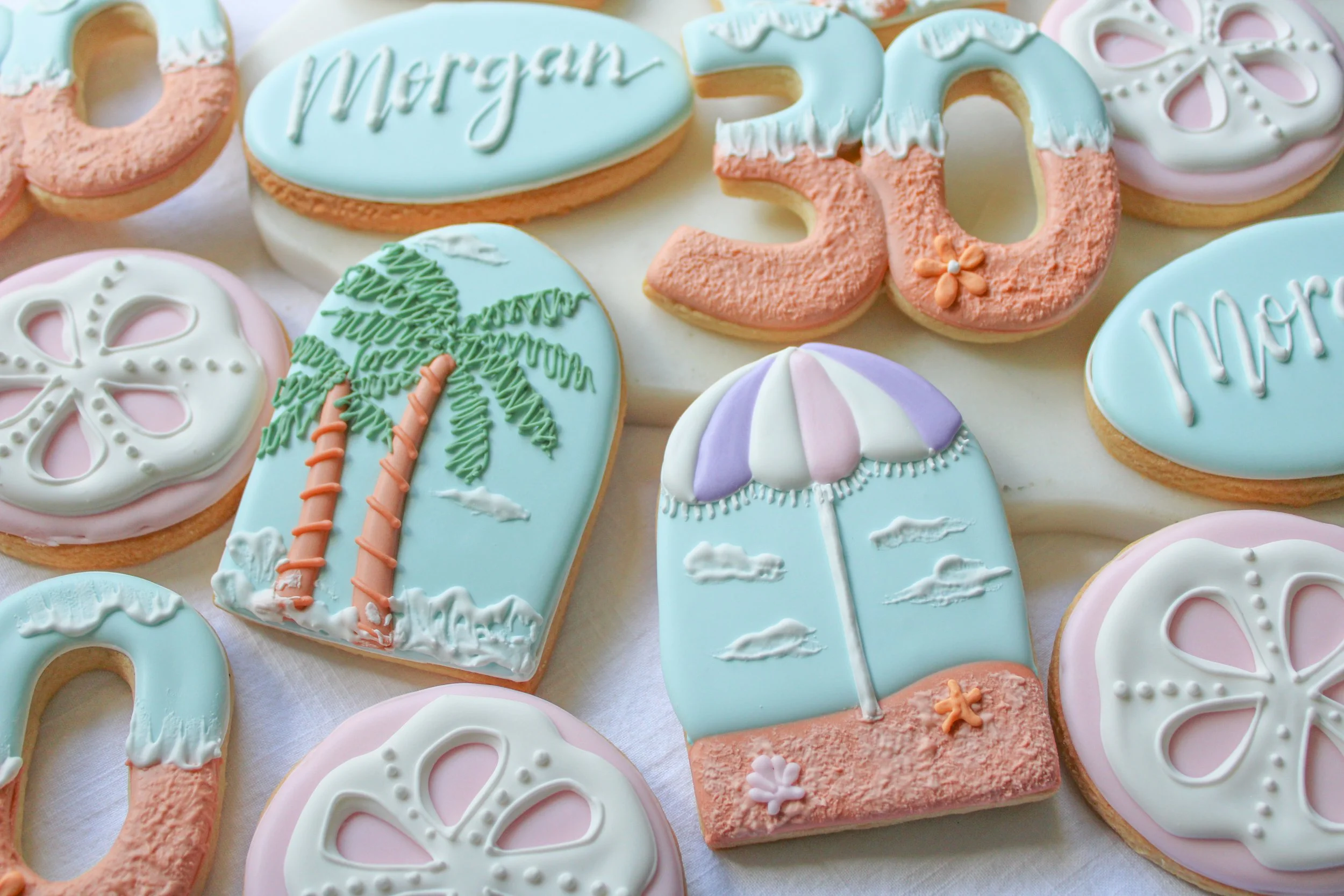 Decorated cookies with pastel icing in shapes of a boat, palm trees, a beach umbrella, and the number 30, for a celebration or birthday.