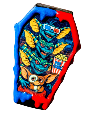 A coffin cake pop with an image inspired by Gremlins 2, surrounded by a blue and red chocolate drip.