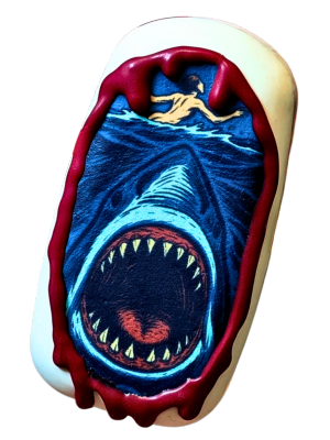 A cake pop decorated with an image inspired by the Jaws movie poster, surrounded by a blood red chocolate drip.