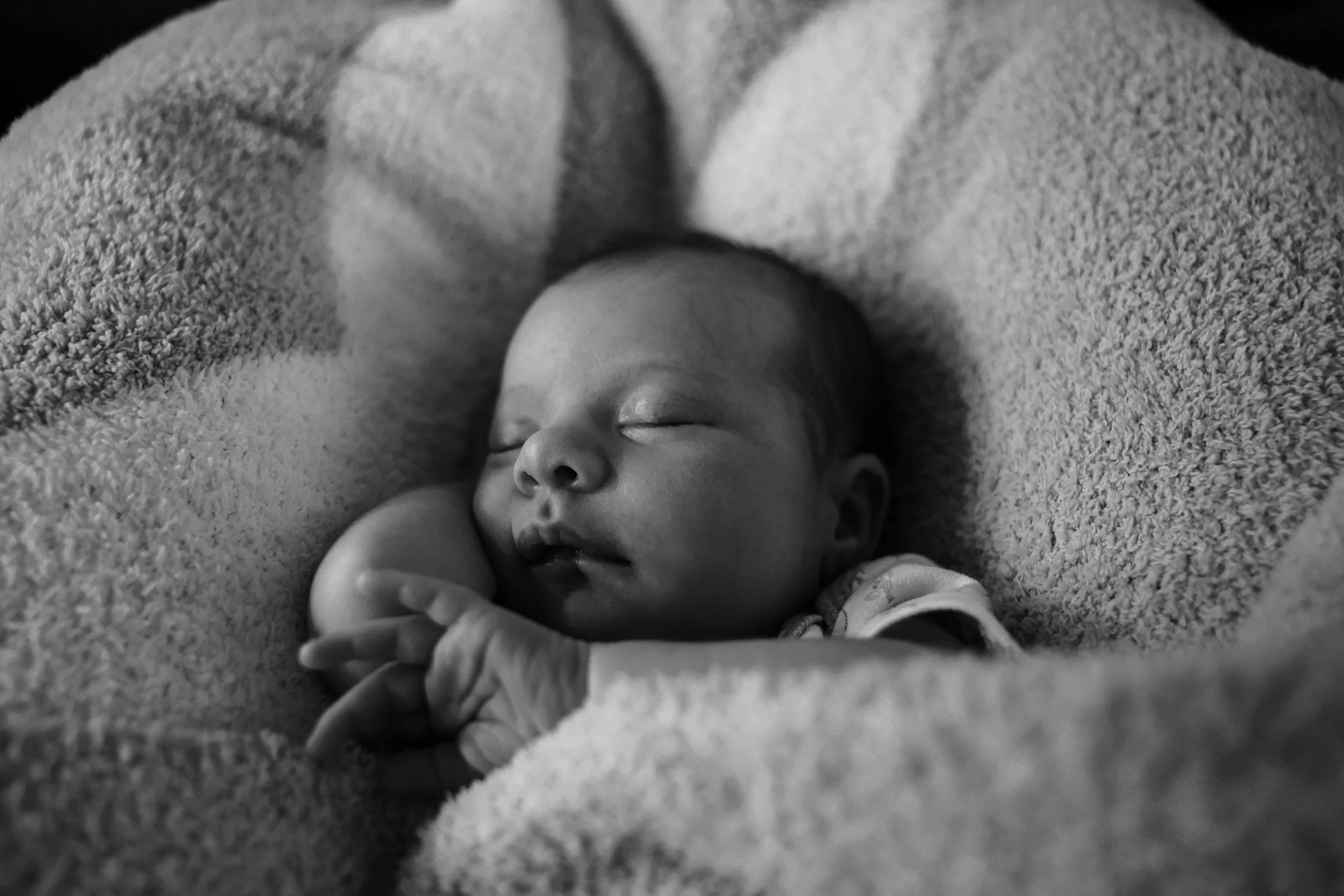 Black and white photo of a sleeping baby wrapped in a blanket, with eyes closed, resting peacefully.