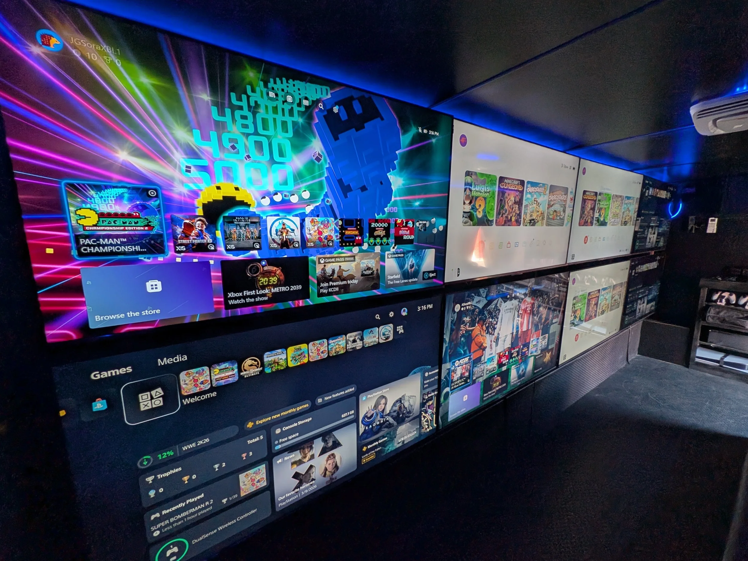 Video game truck interior with a large screen displaying a colorful video game menu, featuring puzzle and arcade game icons, a digital clock, and social media elements, with multiple smaller screens showing game details and options.