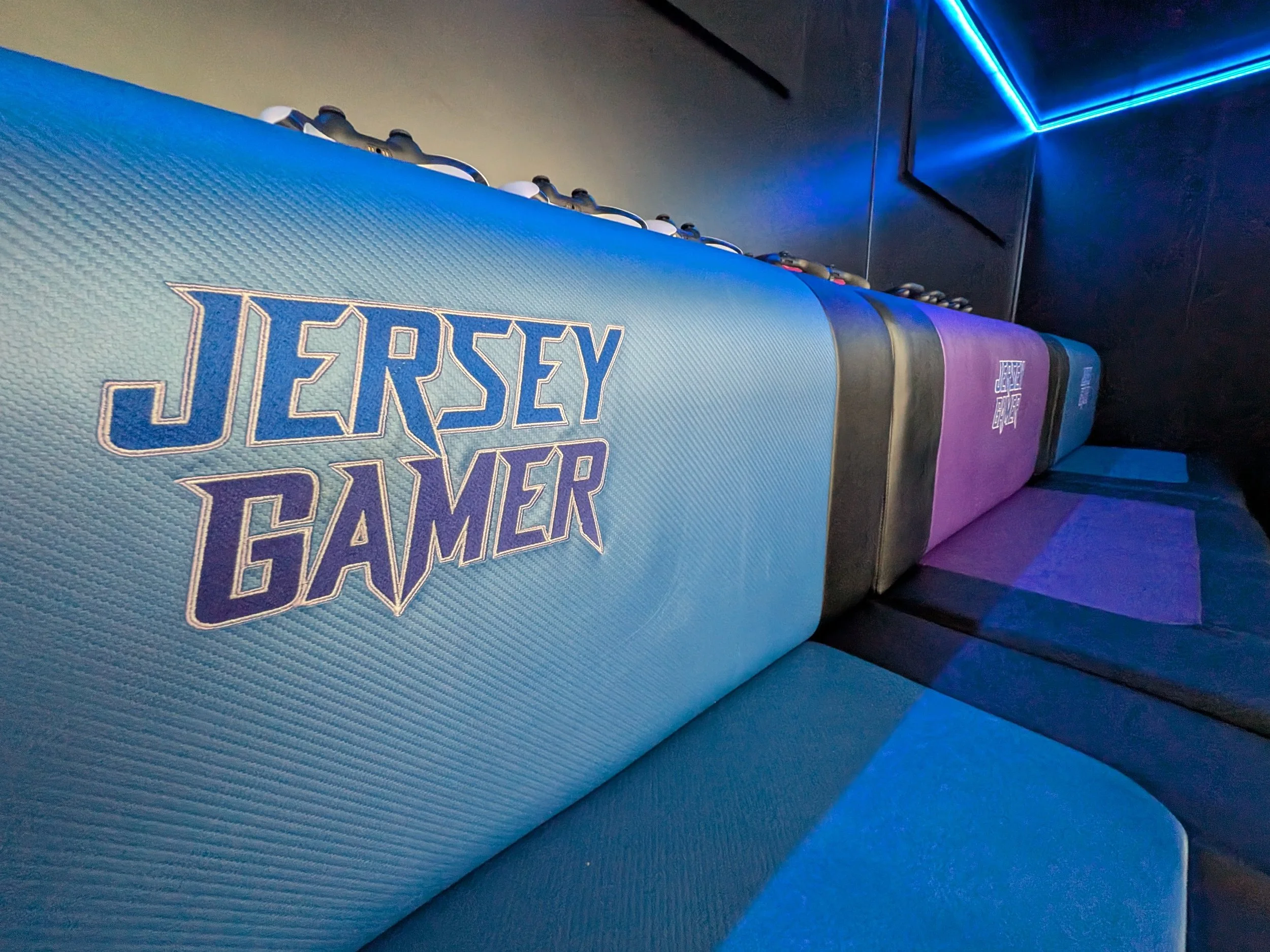 Close-up of a 'Jersey Gamer' branded seat inside a video game truck with purple accents and electric blue lighting in the background.
