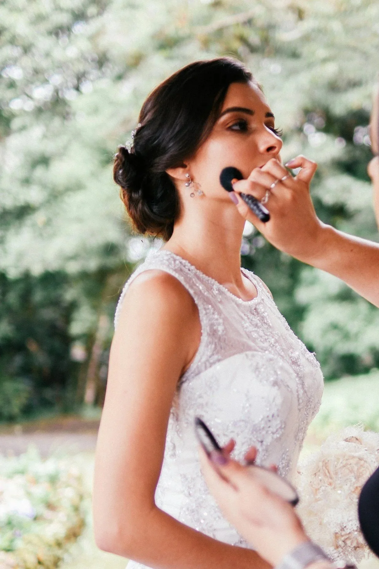 A woman in a wedding dress is getting her makeup done outdoors.