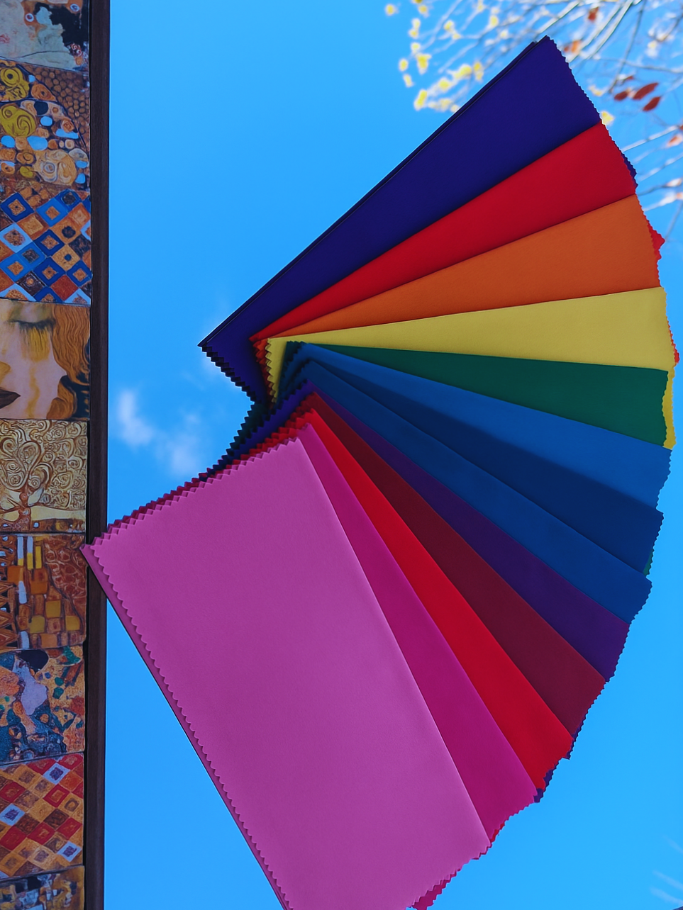 Colorful fabric swatches arranged in a fan shape against a blue sky with few clouds and tree branches.