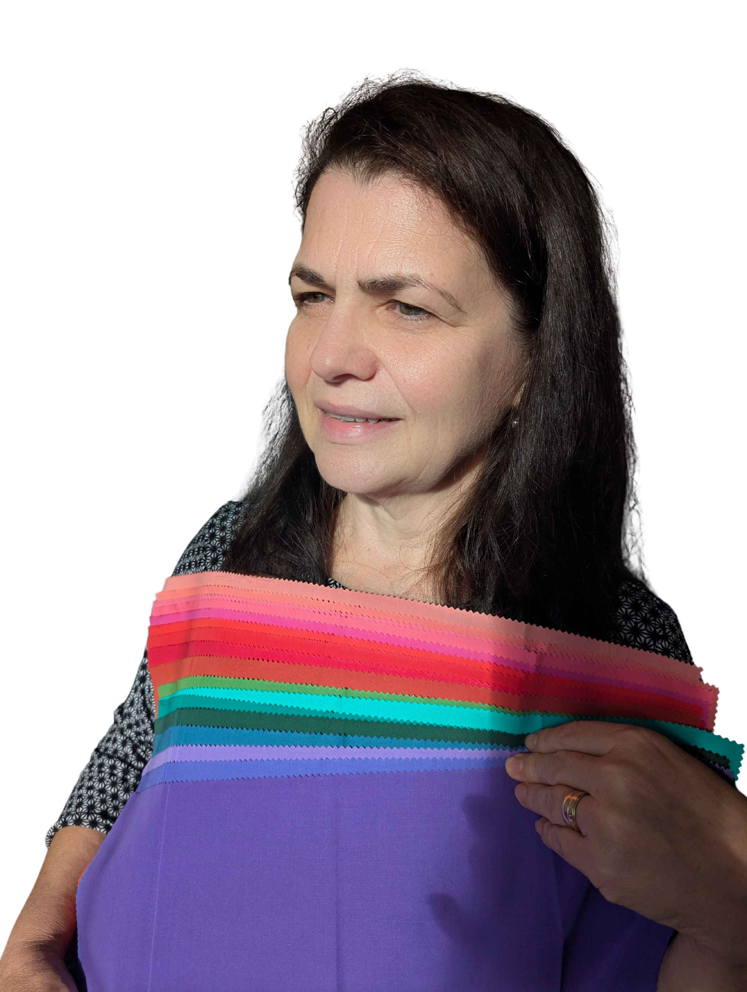 A woman with dark brown hair holding a rainbow-colored fabric with horizontal stripes, wearing a black patterned top, against a black background.