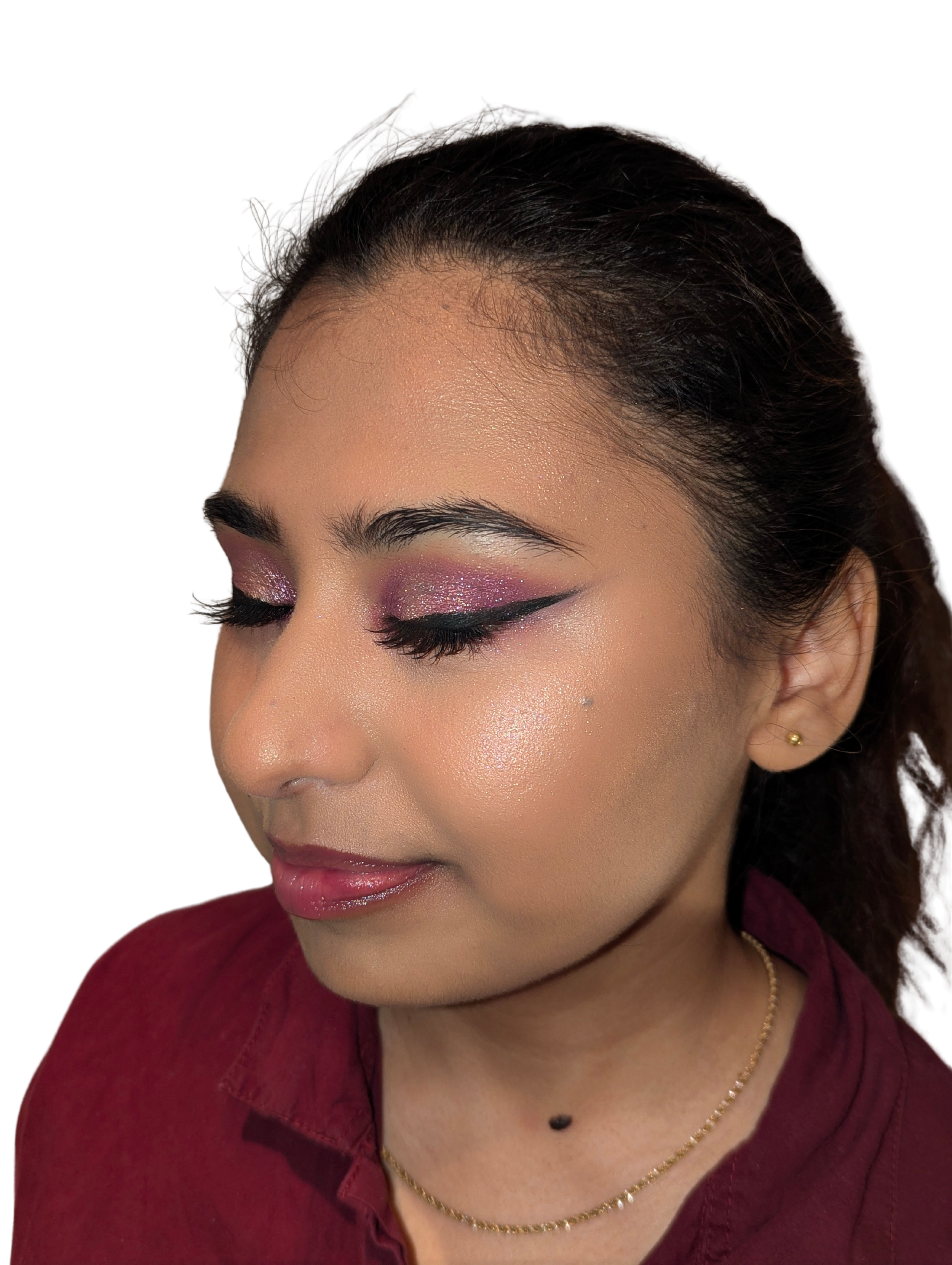 Close-up of a woman with glittery pink and purple eyeshadow, black eyeliner, and glossy lips, wearing gold earrings and a necklace with a marquise-shaped pendant