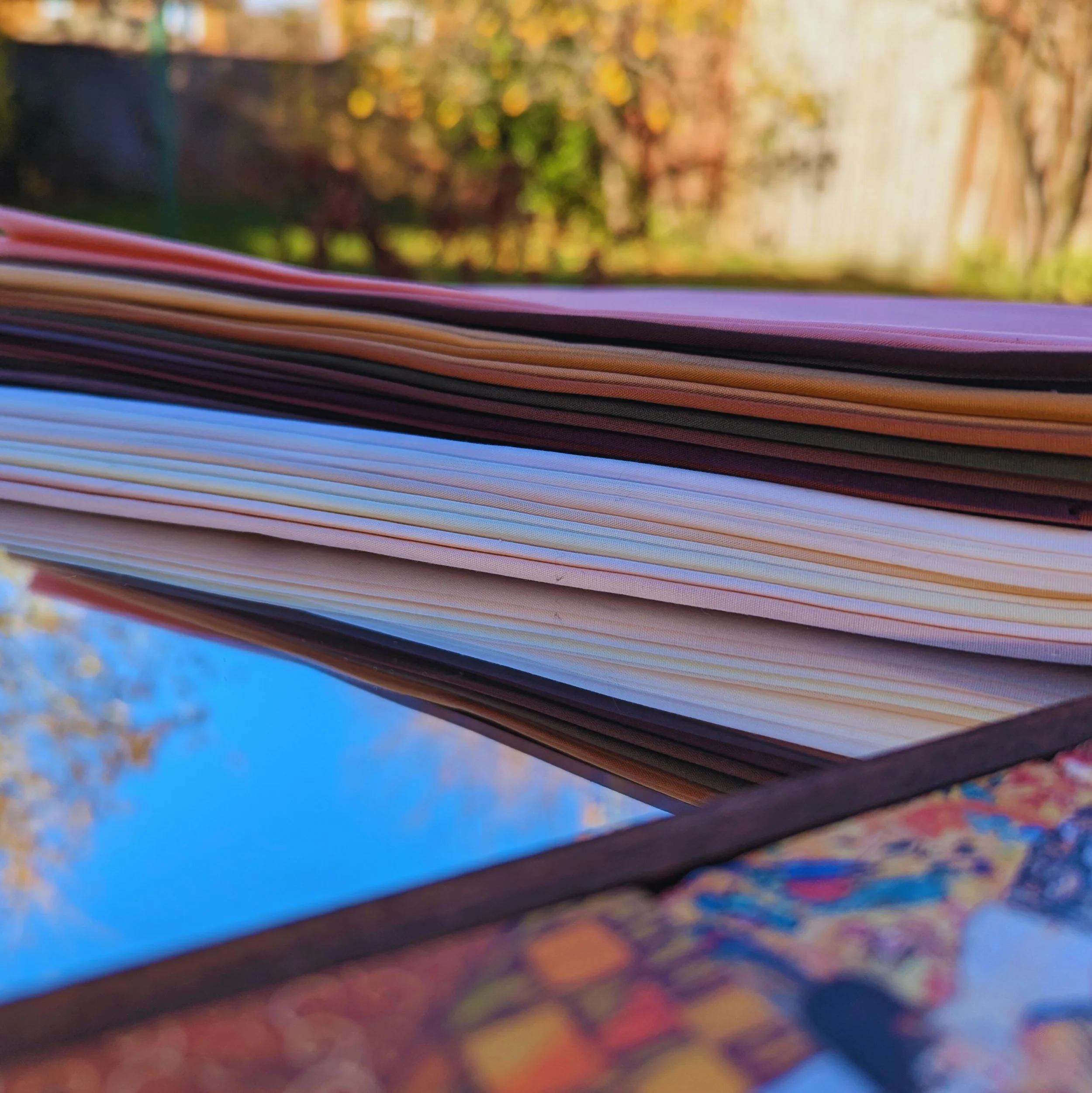 Close-up of a stack of papers or notebooks on a reflective surface outdoors with trees and a wooden fence in the background.