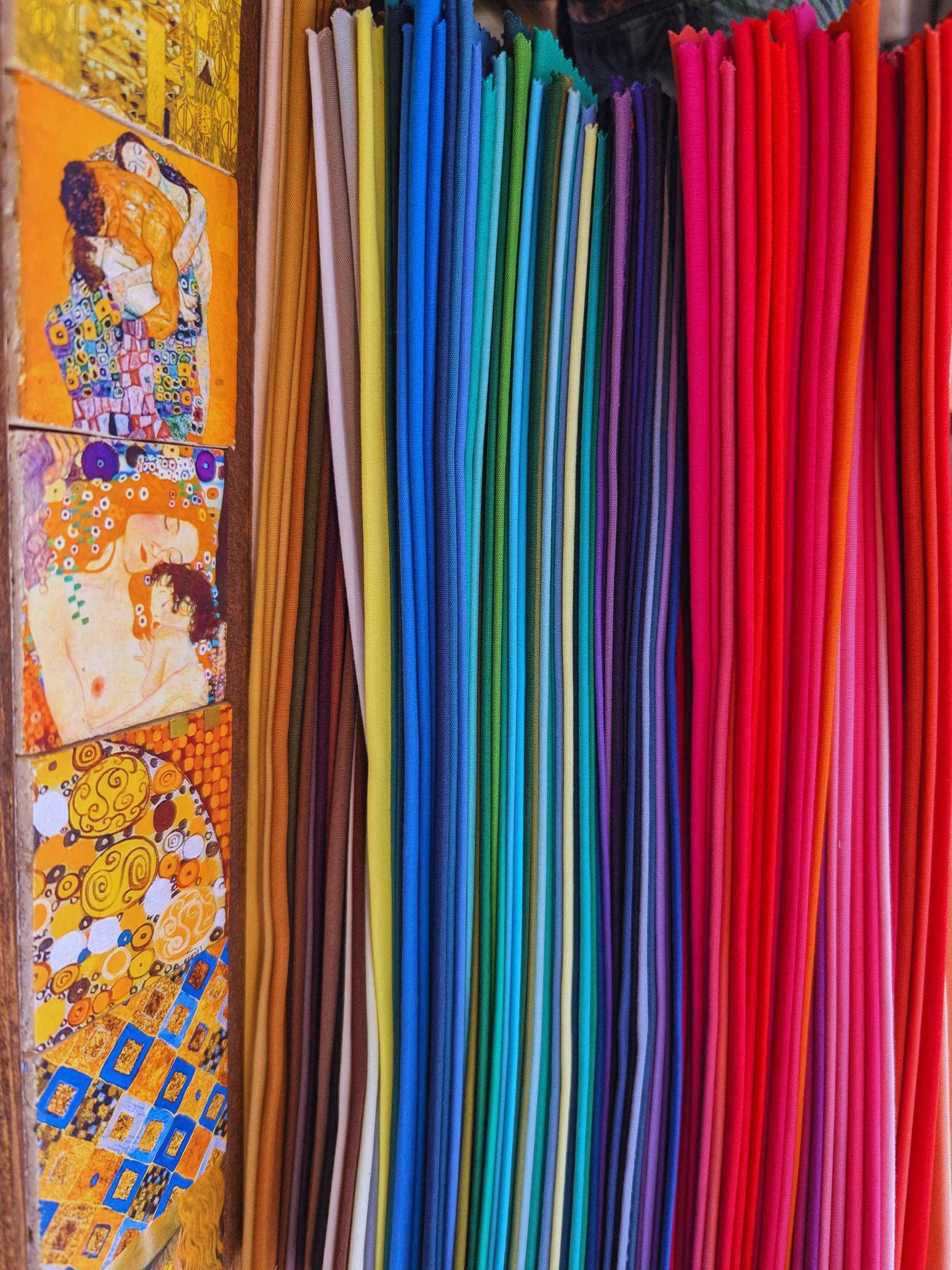 Colorful fabric or paper sticks arranged in a rainbow pattern beside paintings of Klimt's artwork.