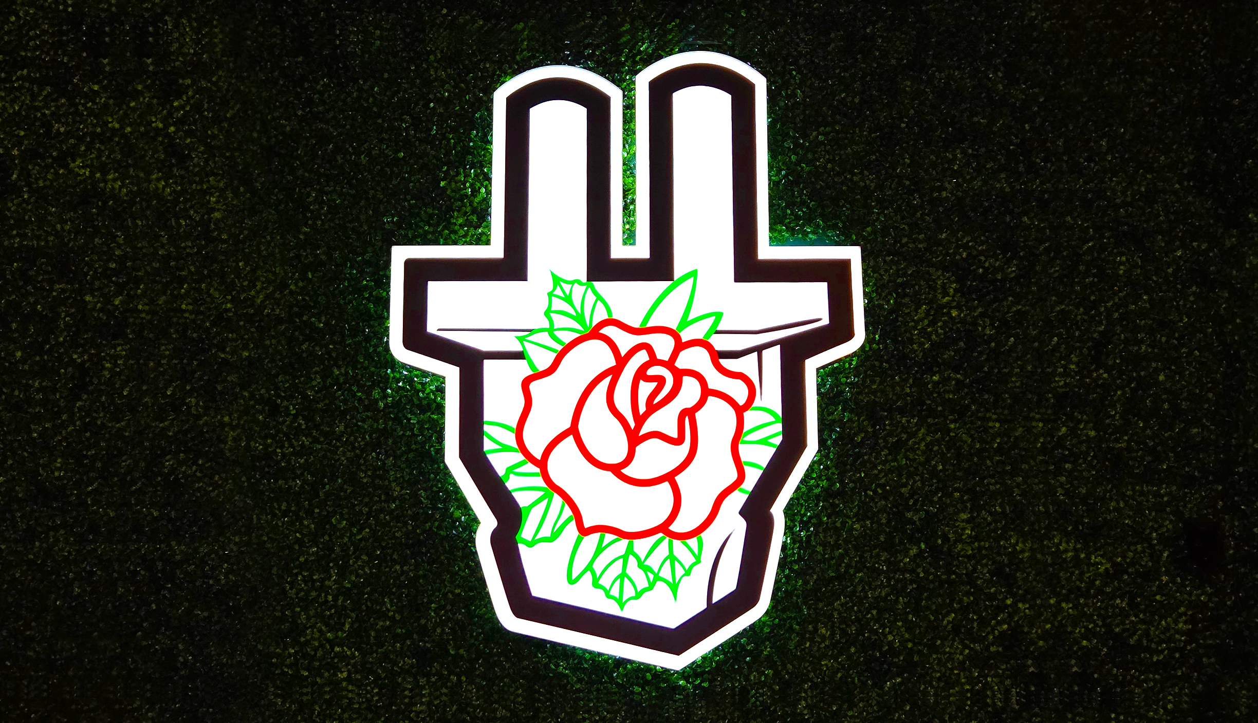 Neon sign featuring a black and white crossed hammer with a red rose and green leaves in the center, mounted on a textured black background.
