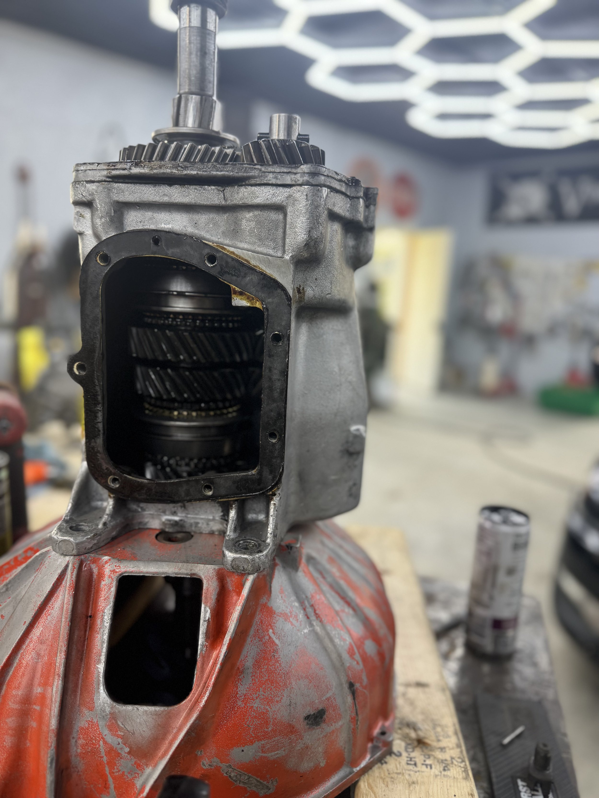 Close-up of an engine component, possibly a transmission or gearbox, mounted on a red base, in a workshop setting.