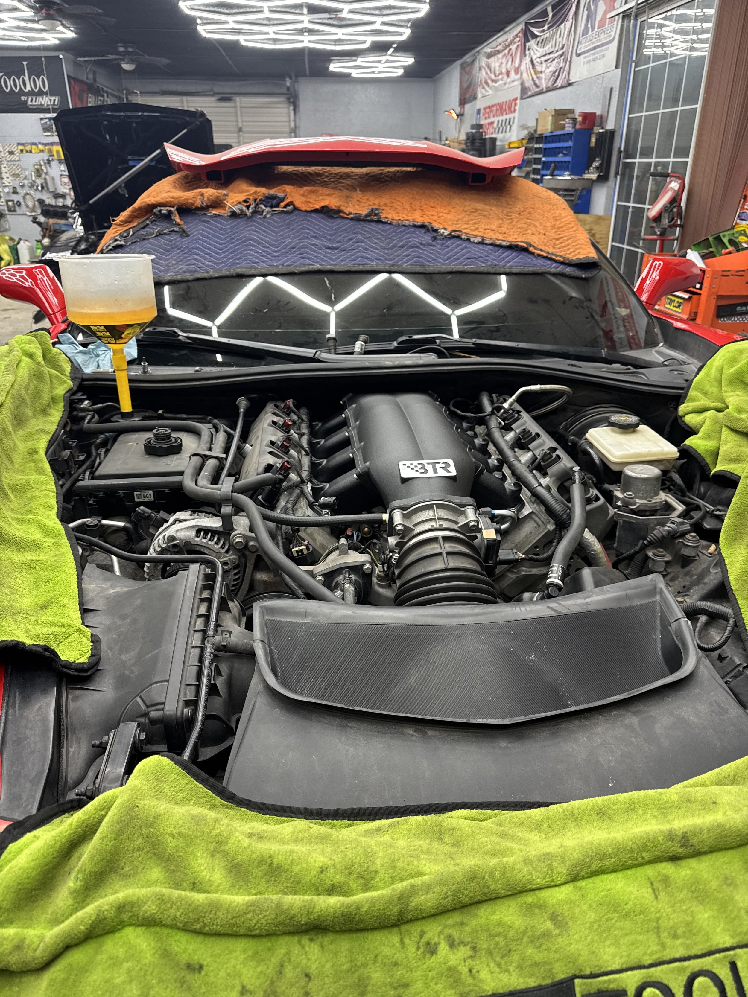 Under the hood of a car in a service garage, with engine components visible and various tools and cloths around, as the car undergoes maintenance or repair.