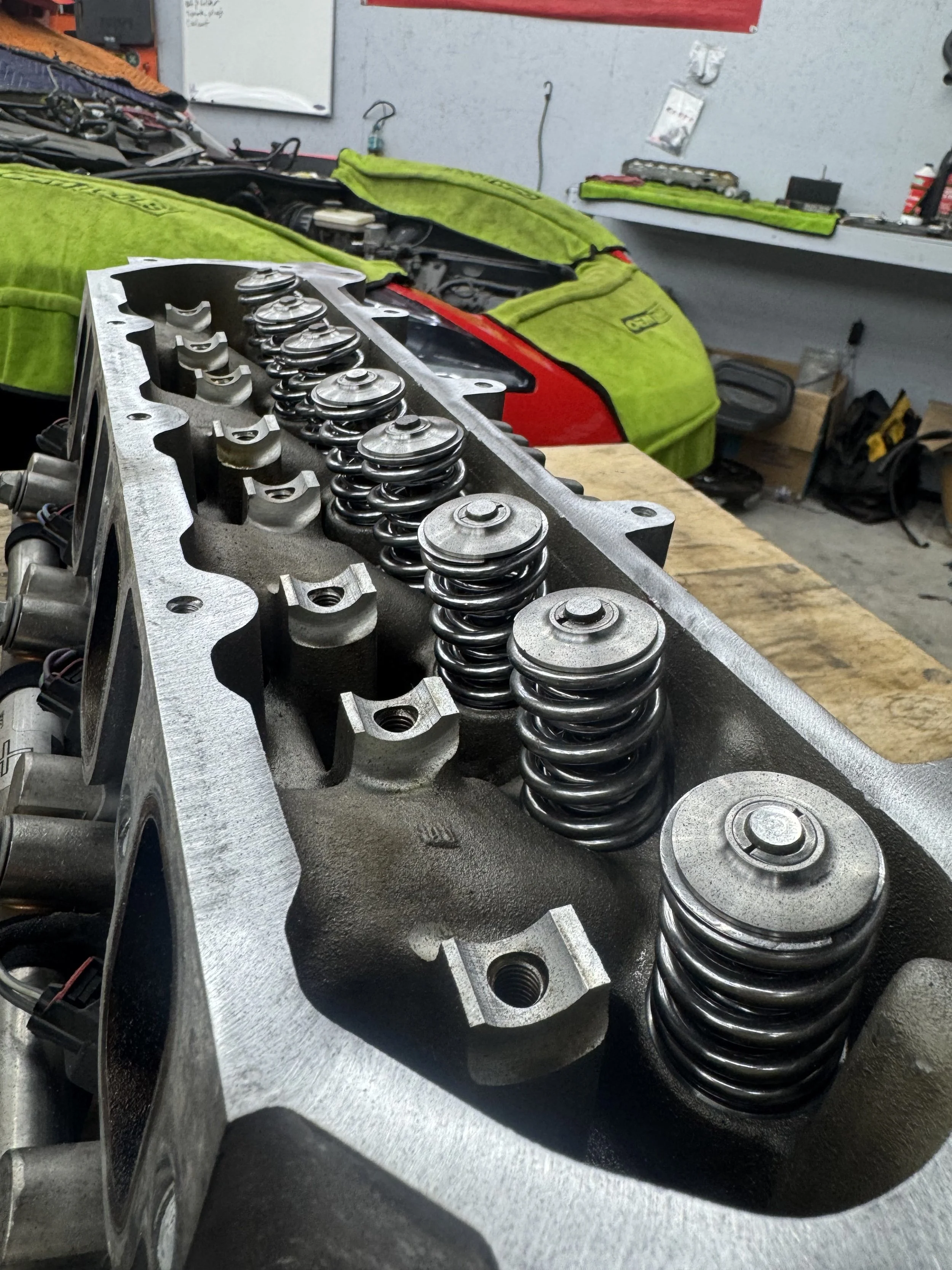 A car engine's cylinder head with valve springs, positioned on a workbench in a repair shop.