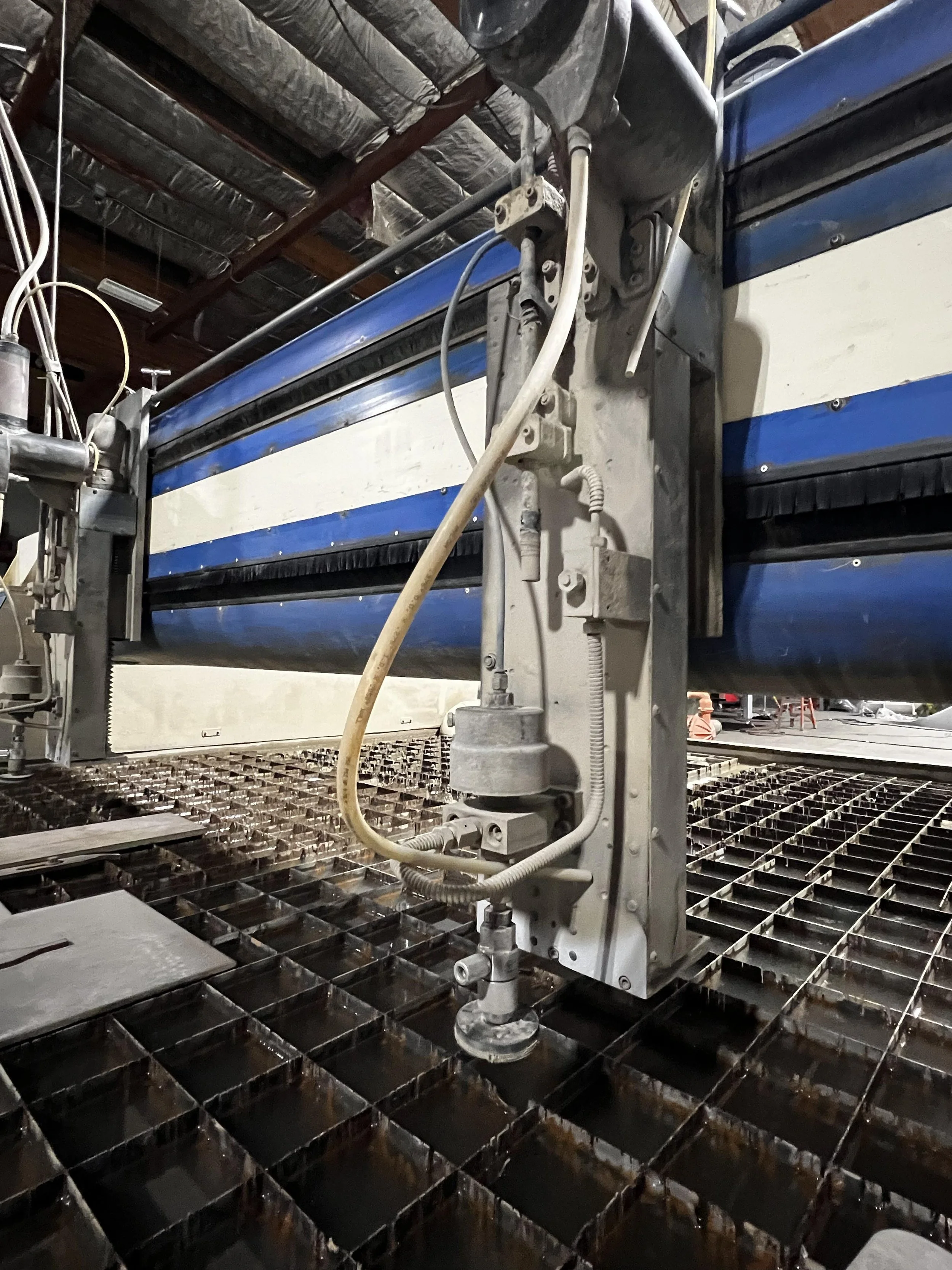 Close-up of industrial machinery on a metal grid floor, with pipes, wires, and structural components.