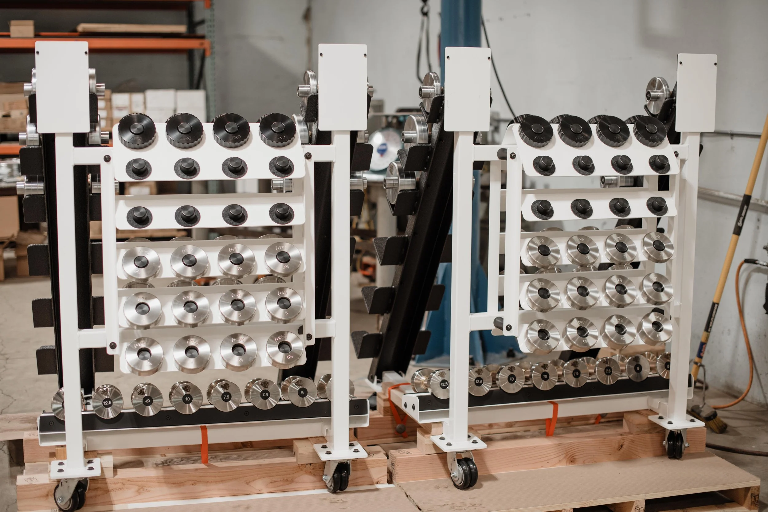 Two white metal frame carts with numerous black and silver knobs mounted on wheels, used for testing or calibration, in a workshop setting.