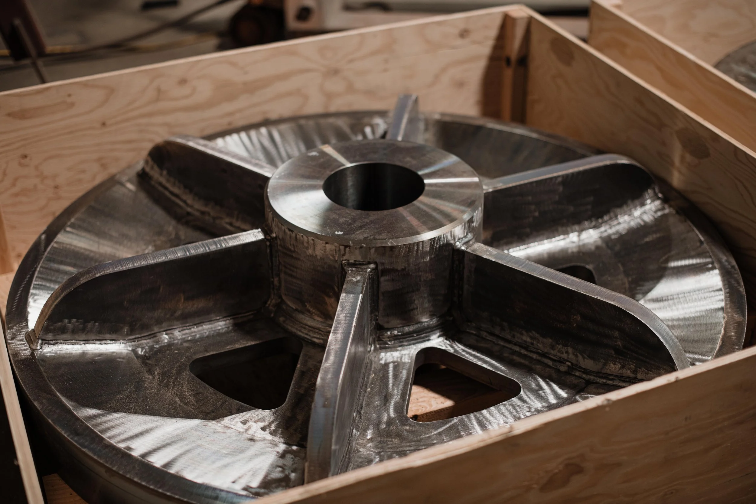 A large metal turbine wheel with multiple blades, resting inside a wooden crate.