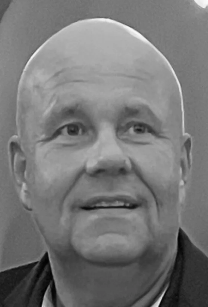 Sort-hvid foto af en mand med skaldet hoved, smilende med rynker og fokus på ansigt.