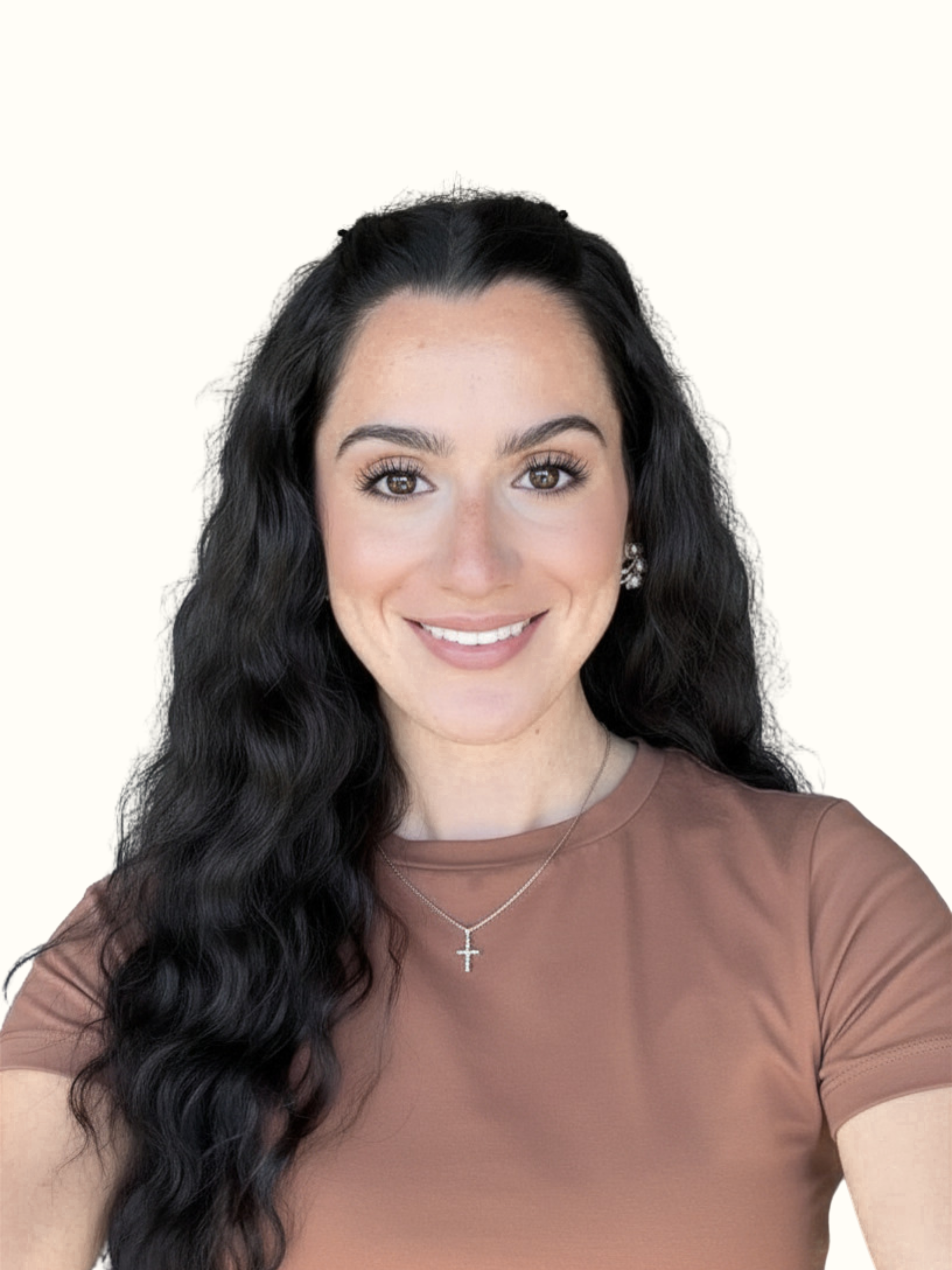 A woman with long, dark wavy hair, wearing a brown shirt, silver earrings, and a cross necklace, smiling against a plain light background.