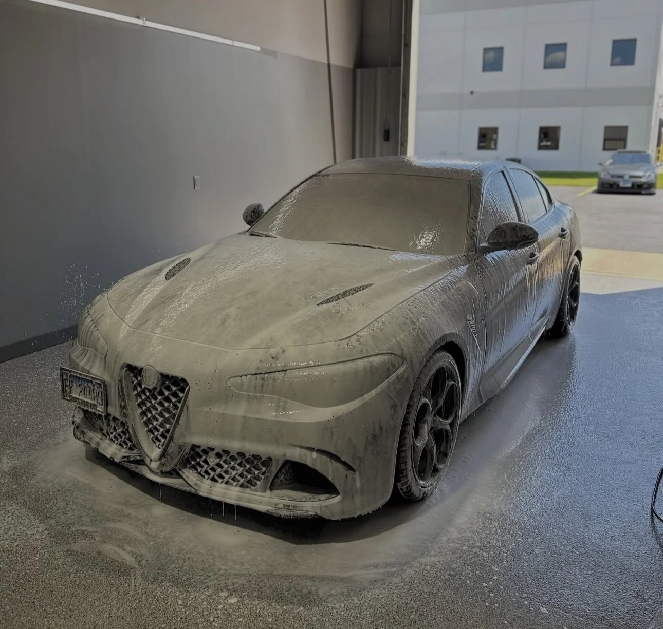 Close-up of a white car with soap foam and shampoo on the tire and side panel during washing.