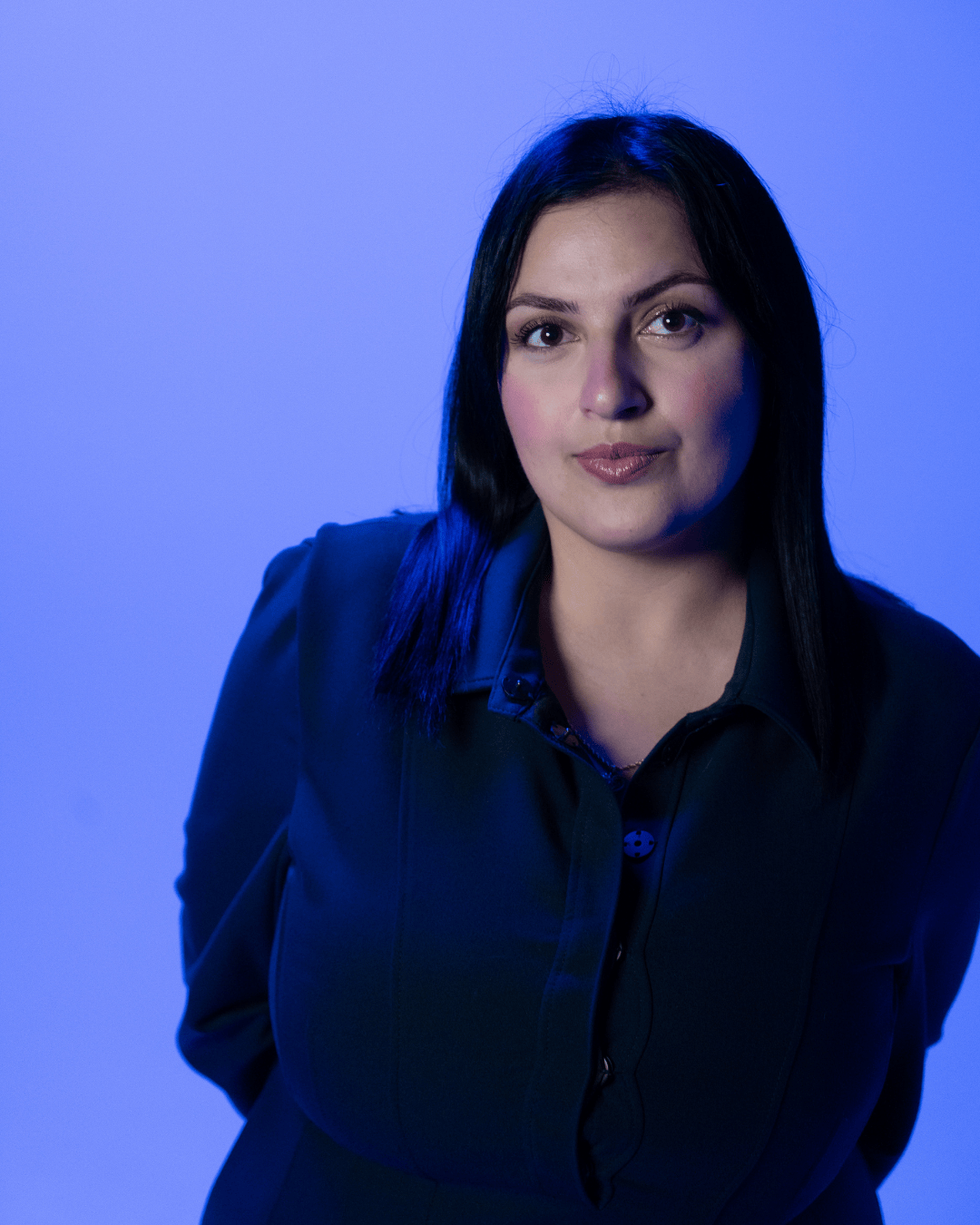 Portrait d'une femme aux cheveux noirs, vêtue d'une veste noire, avec un fond bleu.