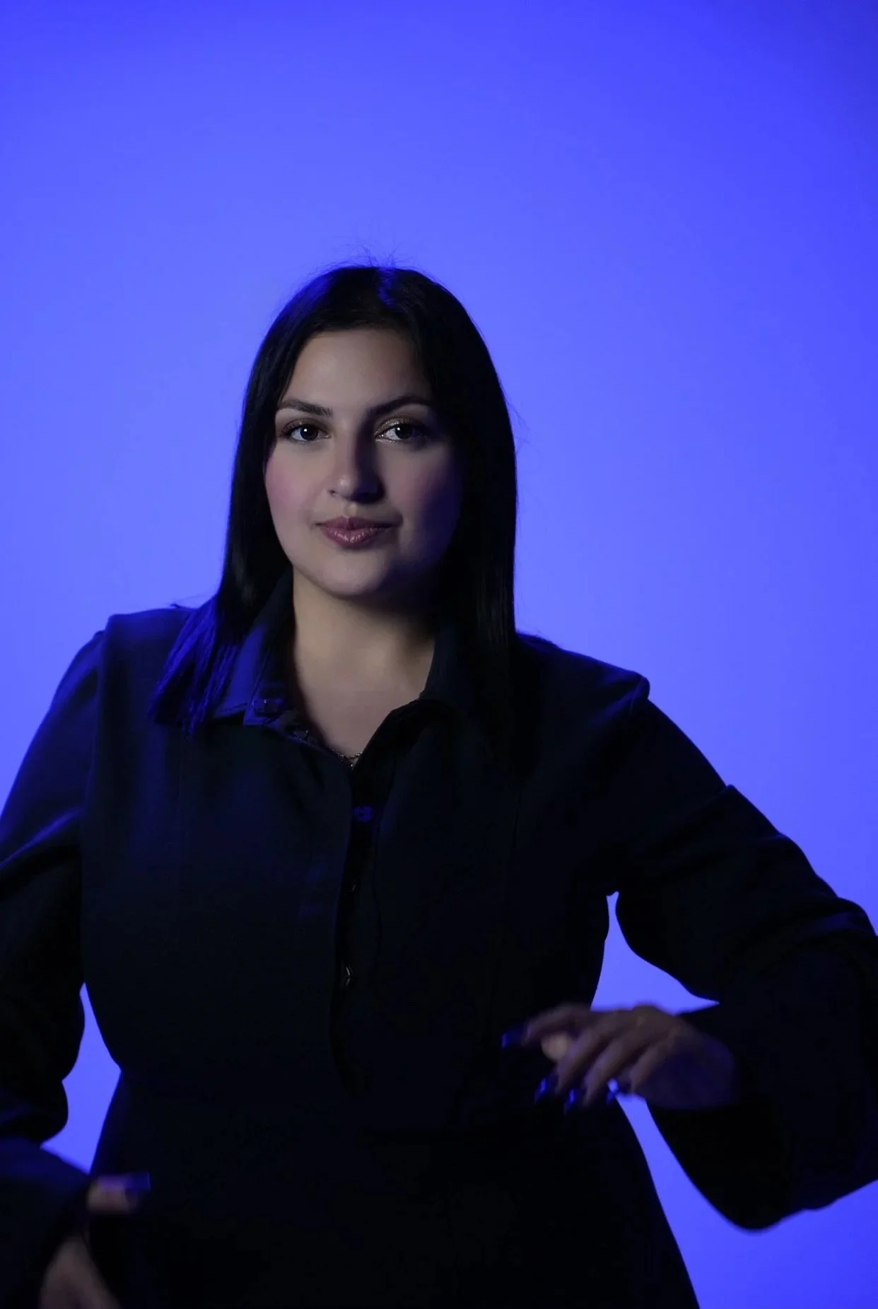 Jeune femme aux cheveux noirs portant une chemise noire avec un fond bleu clair.