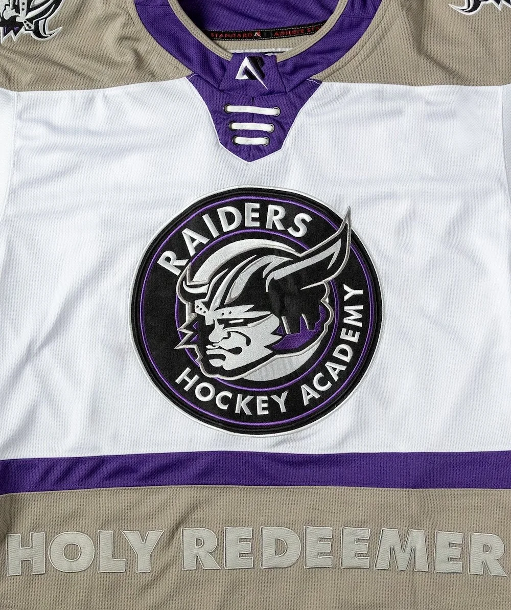 Hockey jersey featuring the Raiders Hockey Academy logo with a Viking warrior, in purple, black, gray, and beige colors. The text 'HOLY REDEEMER' is embroidered at the bottom.