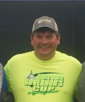 Smiling man wearing a gray cap and neon yellow T-shirt with the text 'Governor's Cup' and a graphic of the Capitol building.