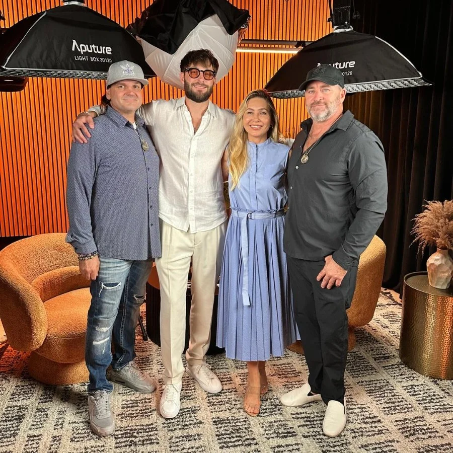 Four people standing in a studio with lighting umbrellas, posing and smiling for a photo.
